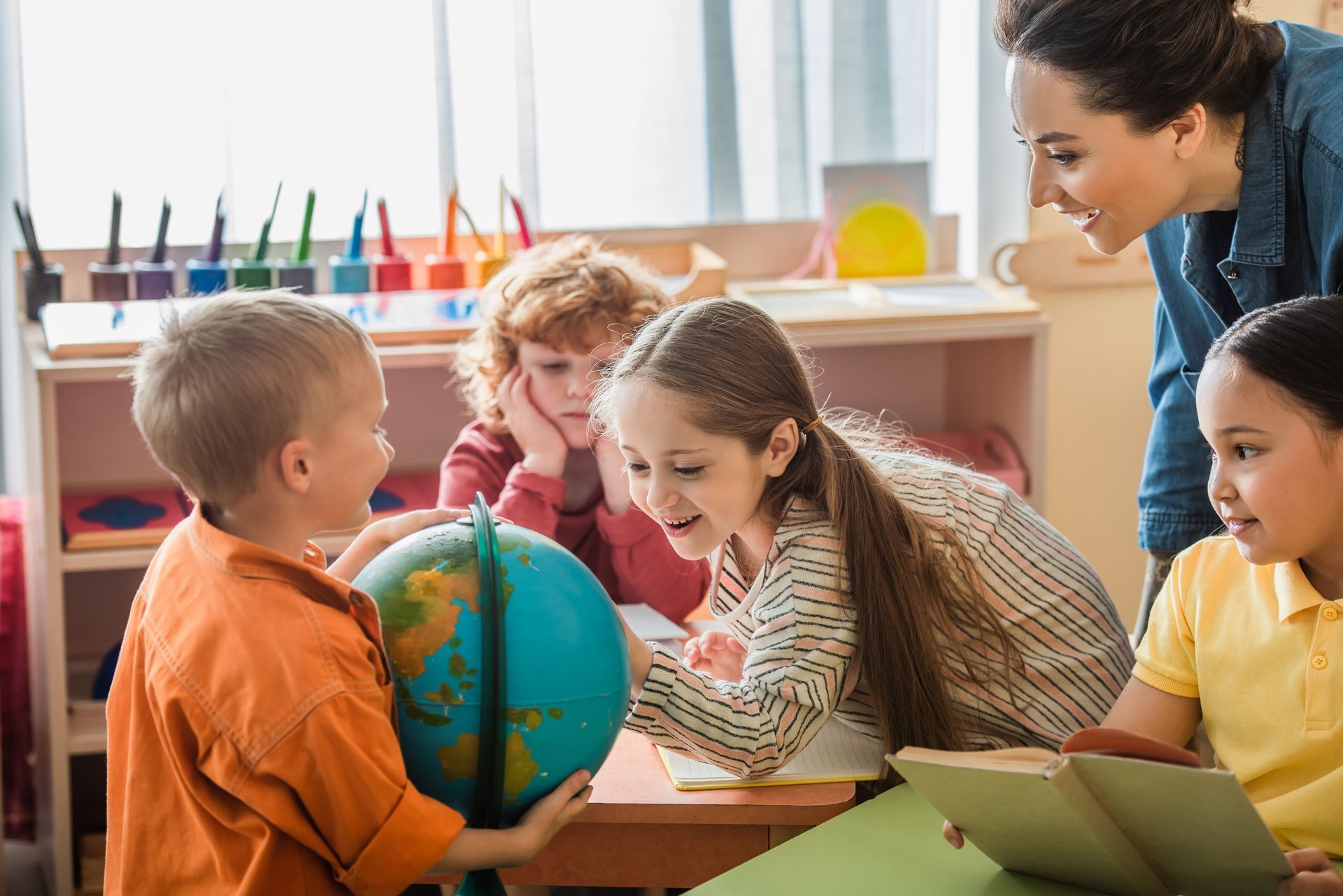 Teacher and children gathered around a globe in a bright classroom, studying together