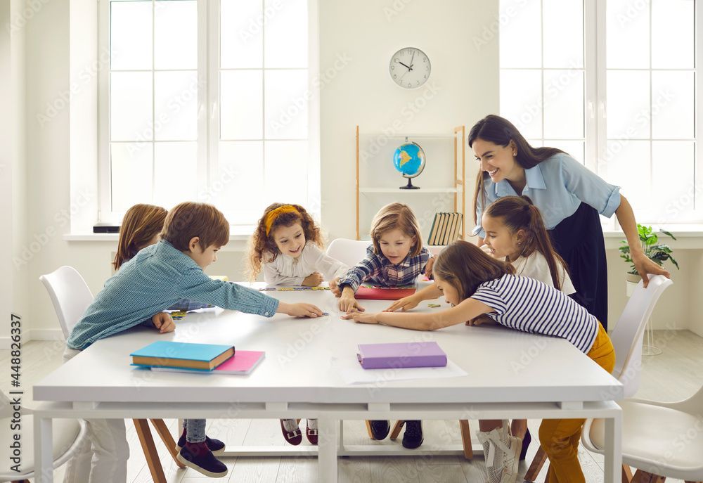 Children gathered around a table in a bright classroom, working on a shared activity with a teacher assisting.