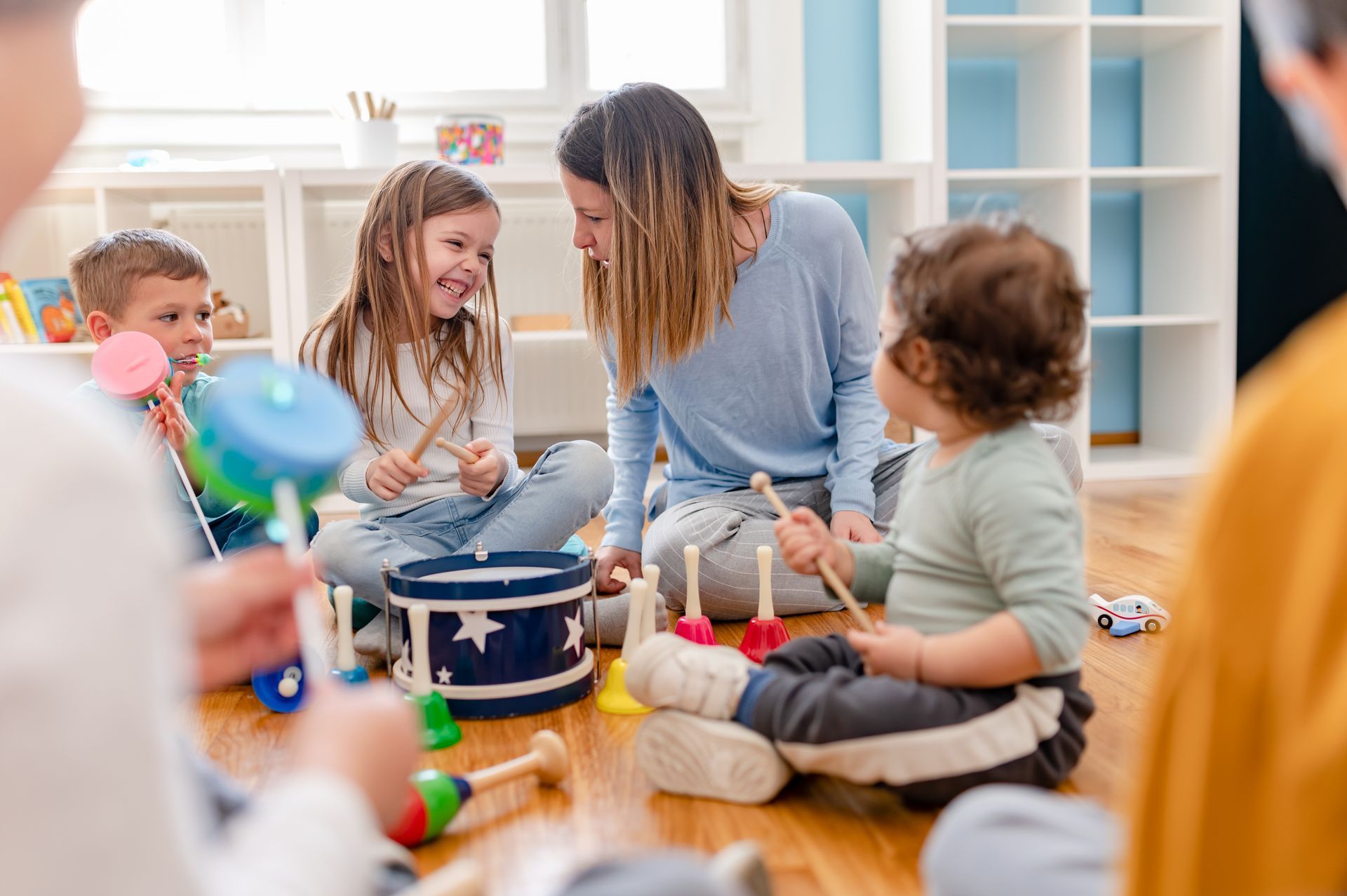 Children and an adult gathered on the floor around a birthday cake with lit candles in a bright room