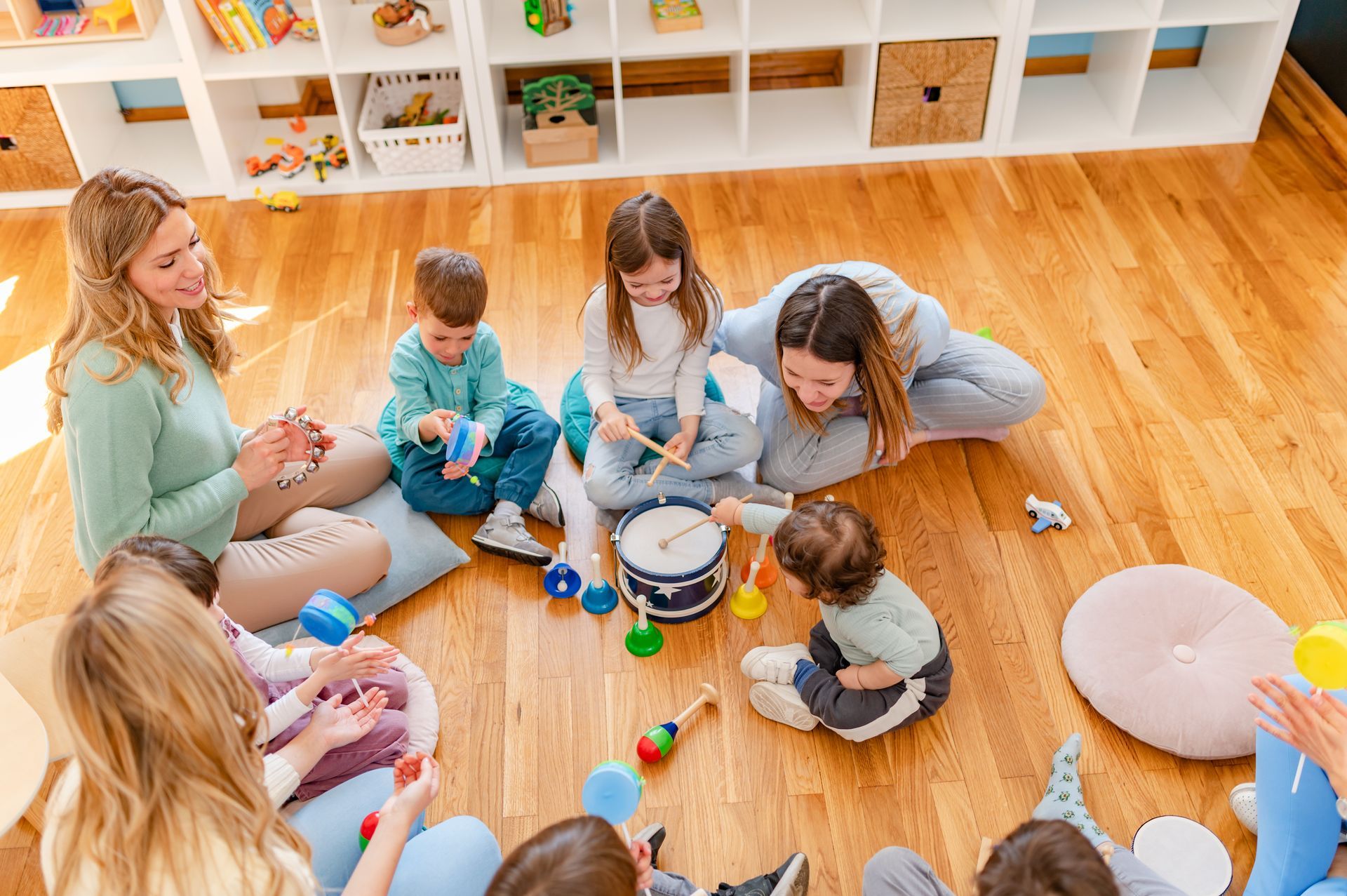 People sitting on a wooden floor playing with toys in a bright playroom