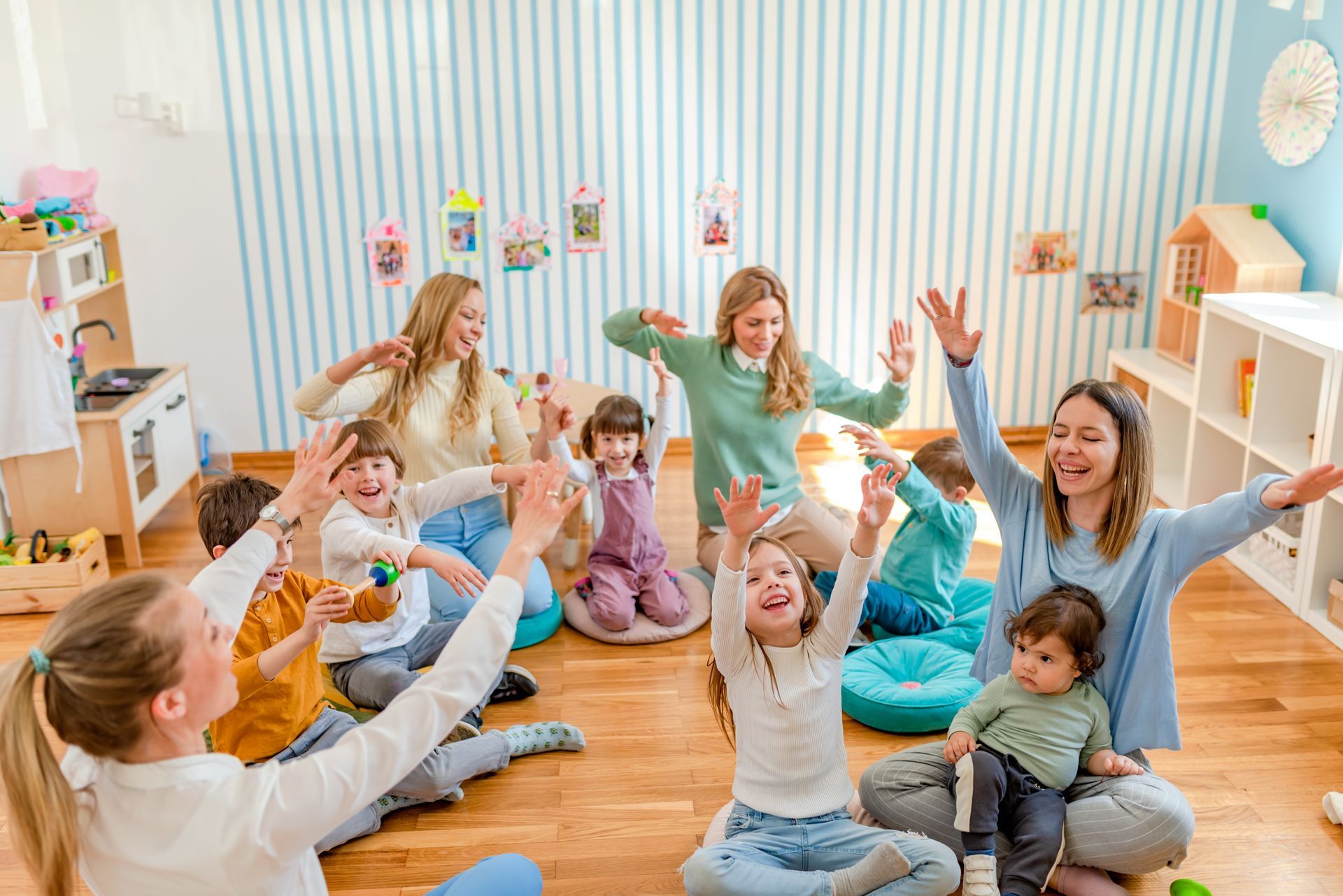 Group of children in a bright classroom playing and sitting on the floor with their hands raised