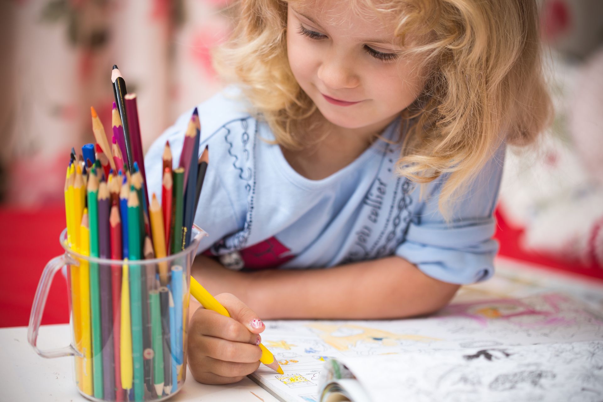 Child drawing with colored pencils at a table, focused on a coloring book