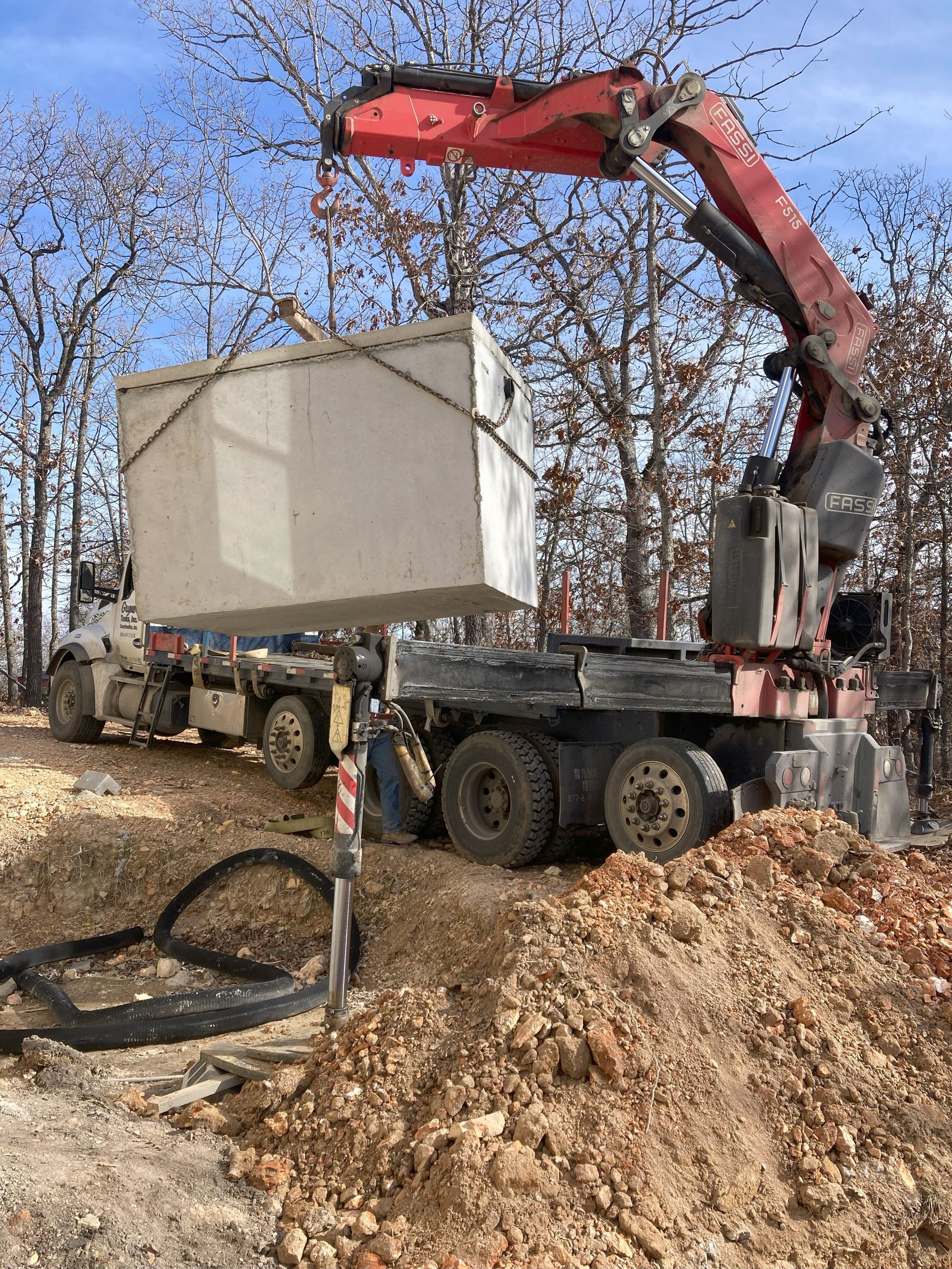 A crane is lifting a large concrete box on top of a truck.