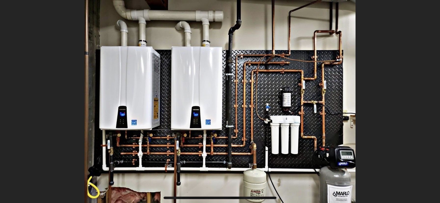 Two white water heaters are hanging on a wall next to copper pipes.