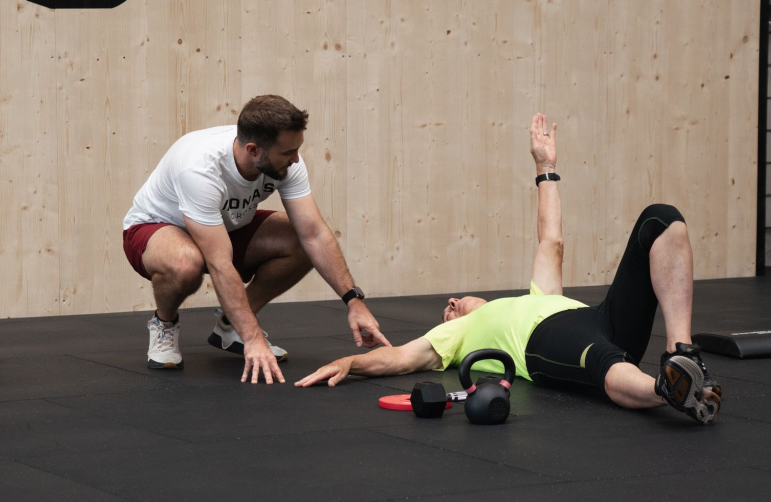Zwei Frauen in schwarzer Sportkleidung trainieren mit Kettlebells in einem Fitnessstudio.