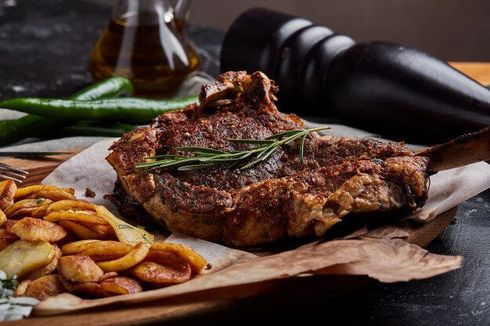 Gegrilltes Steak mit Bratkartoffeln, grünen Chilischoten, Olivenöl und Pfeffermühle auf Holz.