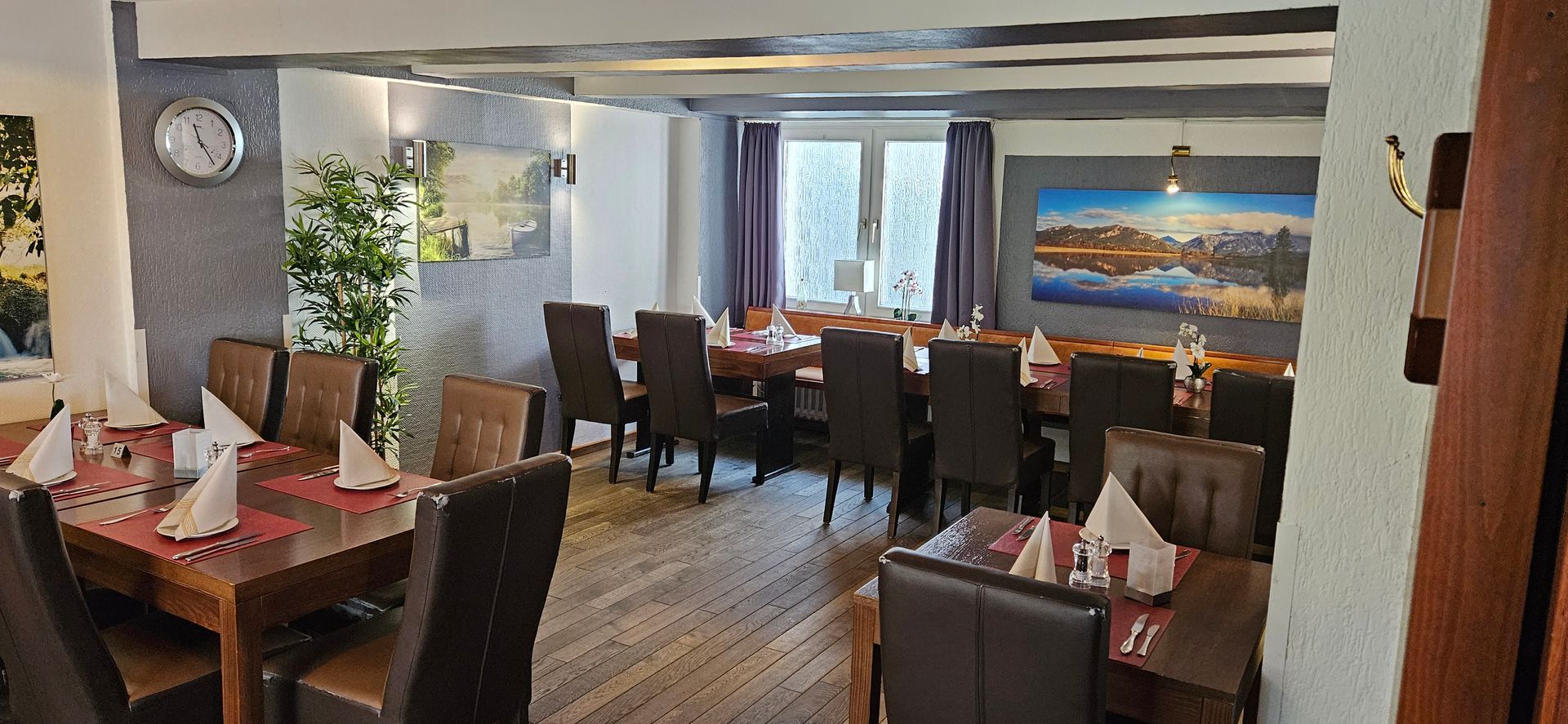 Restaurant-Essbereich mit für Gäste gedeckten Tischen. Dunkle Holztische und -stühle und sanfte Beleuchtung.