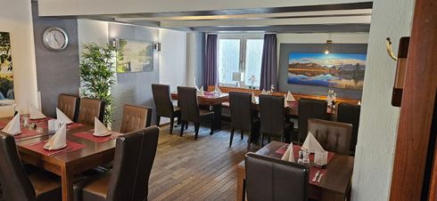 Restaurant-Essbereich mit für Gäste gedeckten Tischen. Dunkle Holztische und -stühle und sanfte Beleuchtung.