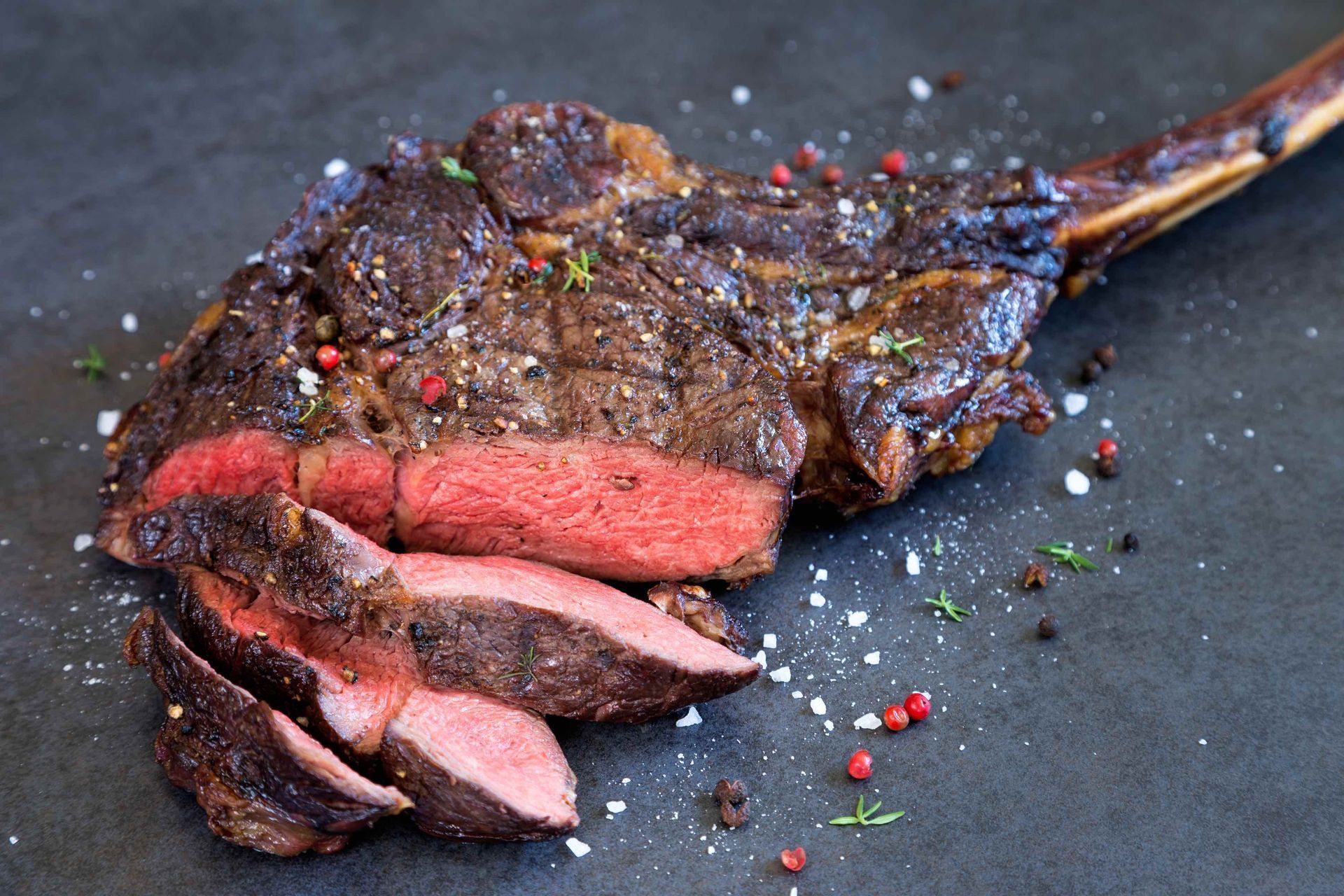 In Scheiben geschnittenes, scharf angebratenes Tomahawk-Steak mit sichtbarem rosa Kern, auf dunklem Untergrund.