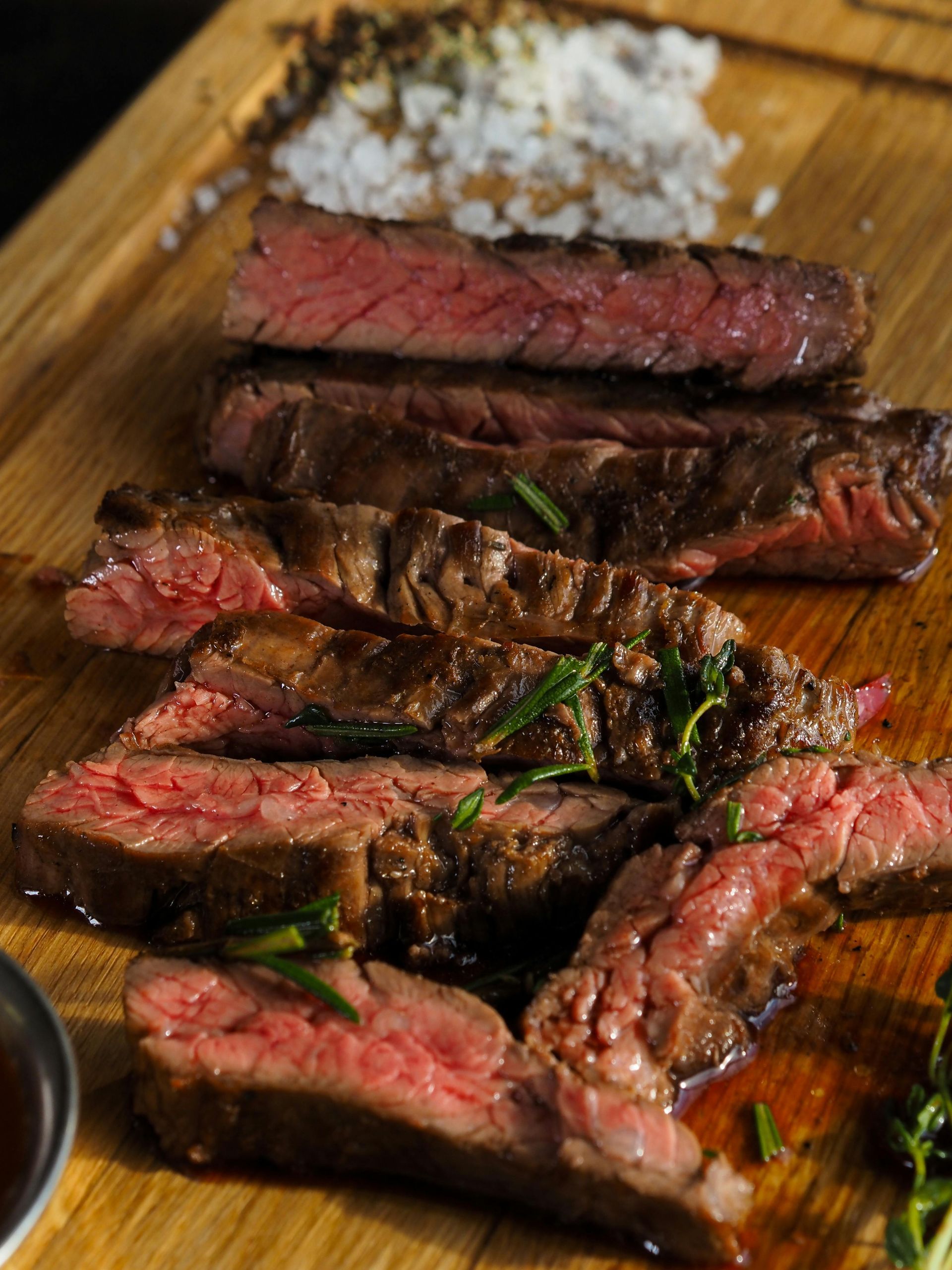 Auf einem Holzbrett angerichtetes, medium-rare gebratenes Steak, garniert mit Rosmarin und Salz.