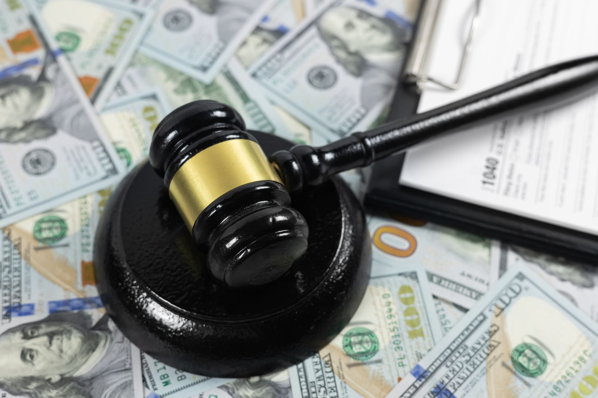 Judge’s gavel on a black base over scattered dollar bills and a pen, symbolizing law and money Judge’s gavel on a black base over scattered dollar bills and a pen, symbolizing law and money