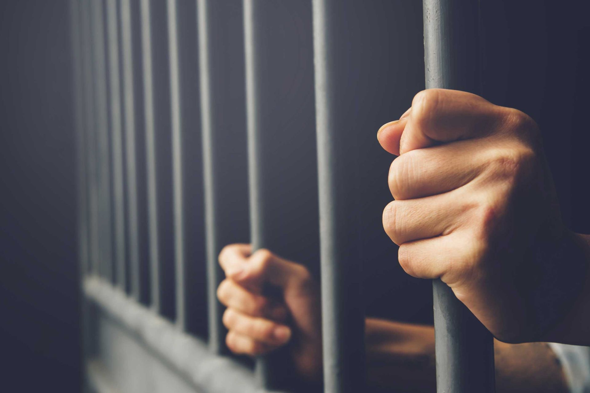 Hands gripping prison bars in a dim jail cell