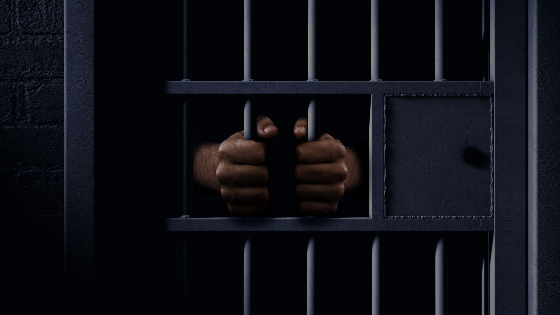 Hands gripping prison bars in a dark cell