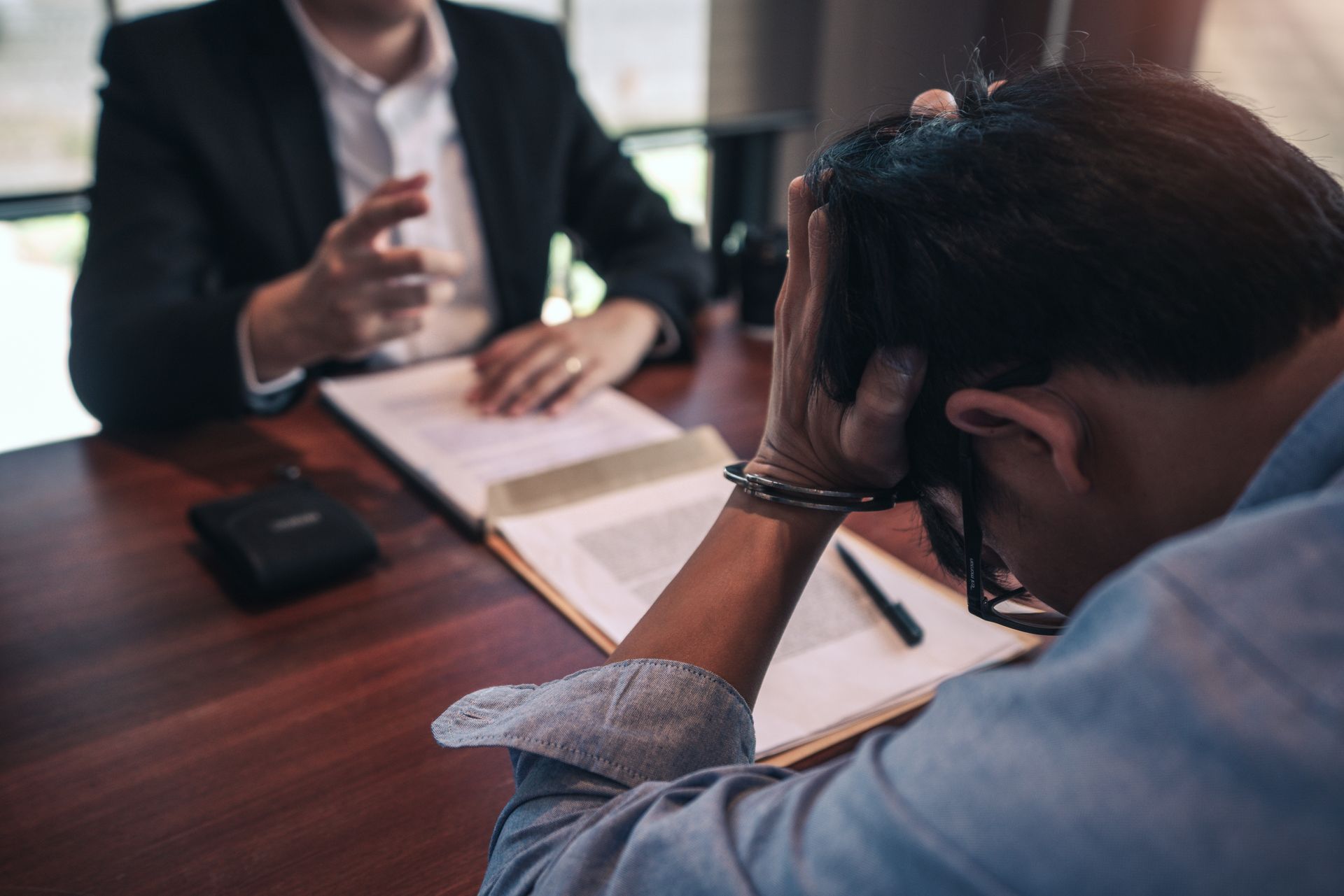 Man in handcuffs, head in hands, sits at a table with an attorney reviewing documents.