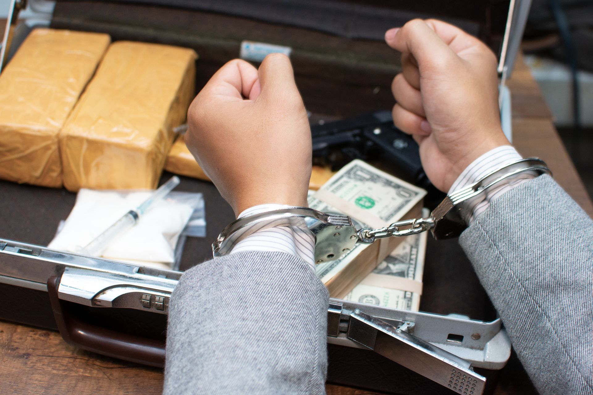 Person in handcuffs with briefcase containing drugs, cash, and a gun.
