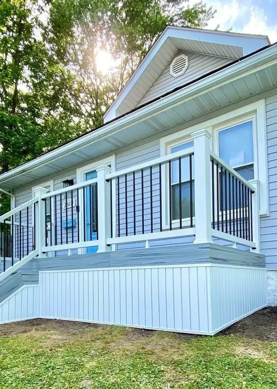 Exterior view of a house with a gray deck and white siding. Black railing and bright sky.