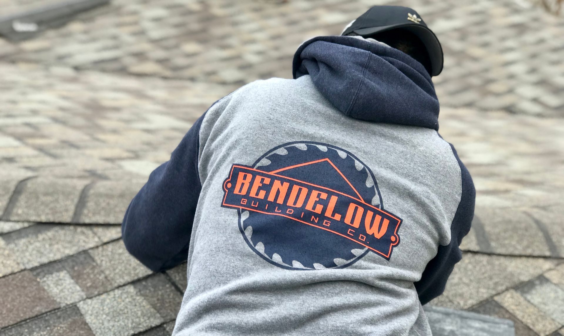 Roofer on a roof wearing a sweatshirt with "Bendelow Building Co." logo on the back.