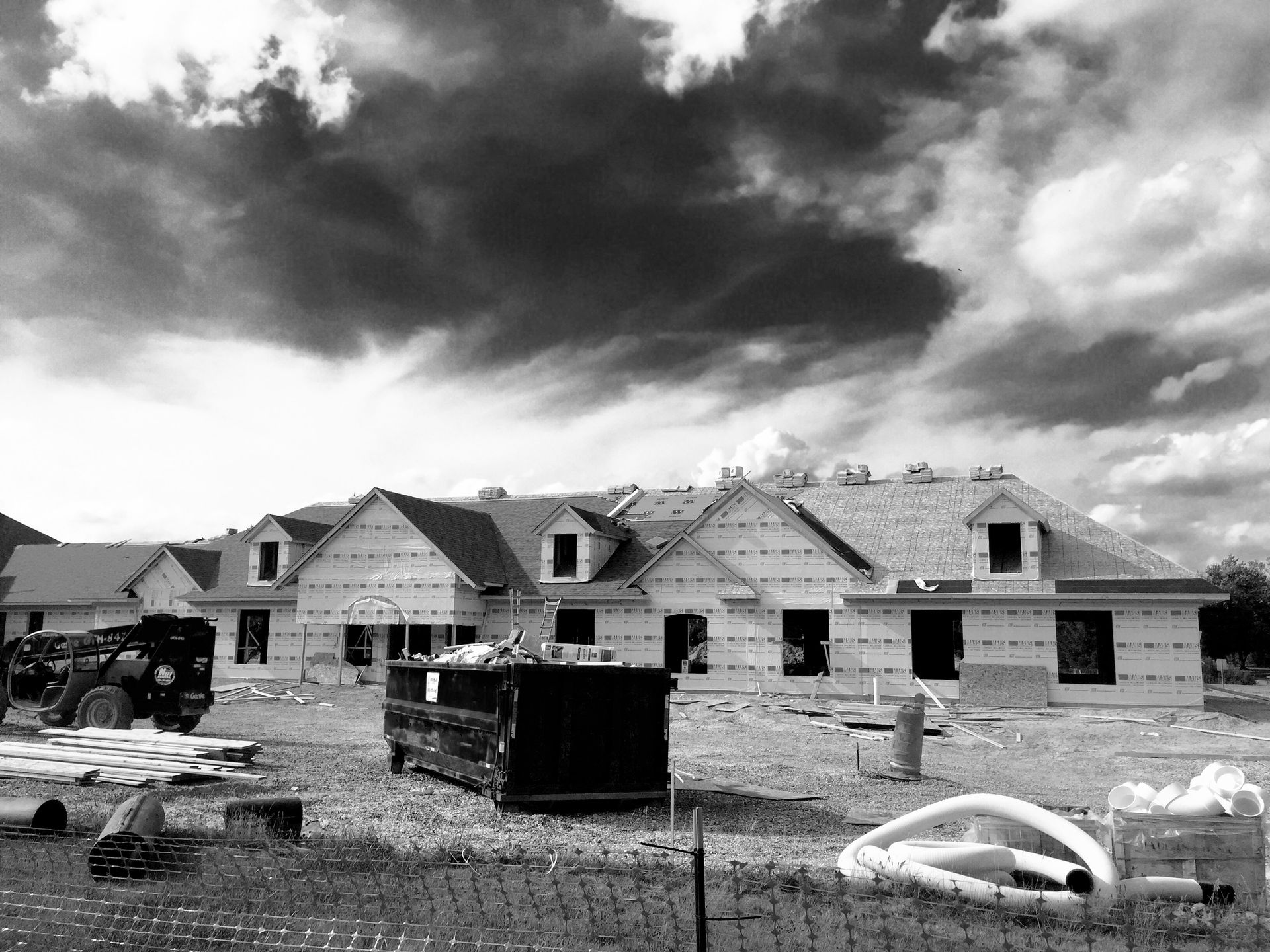 Houses under construction with unfinished rooflines against a cloudy sky.