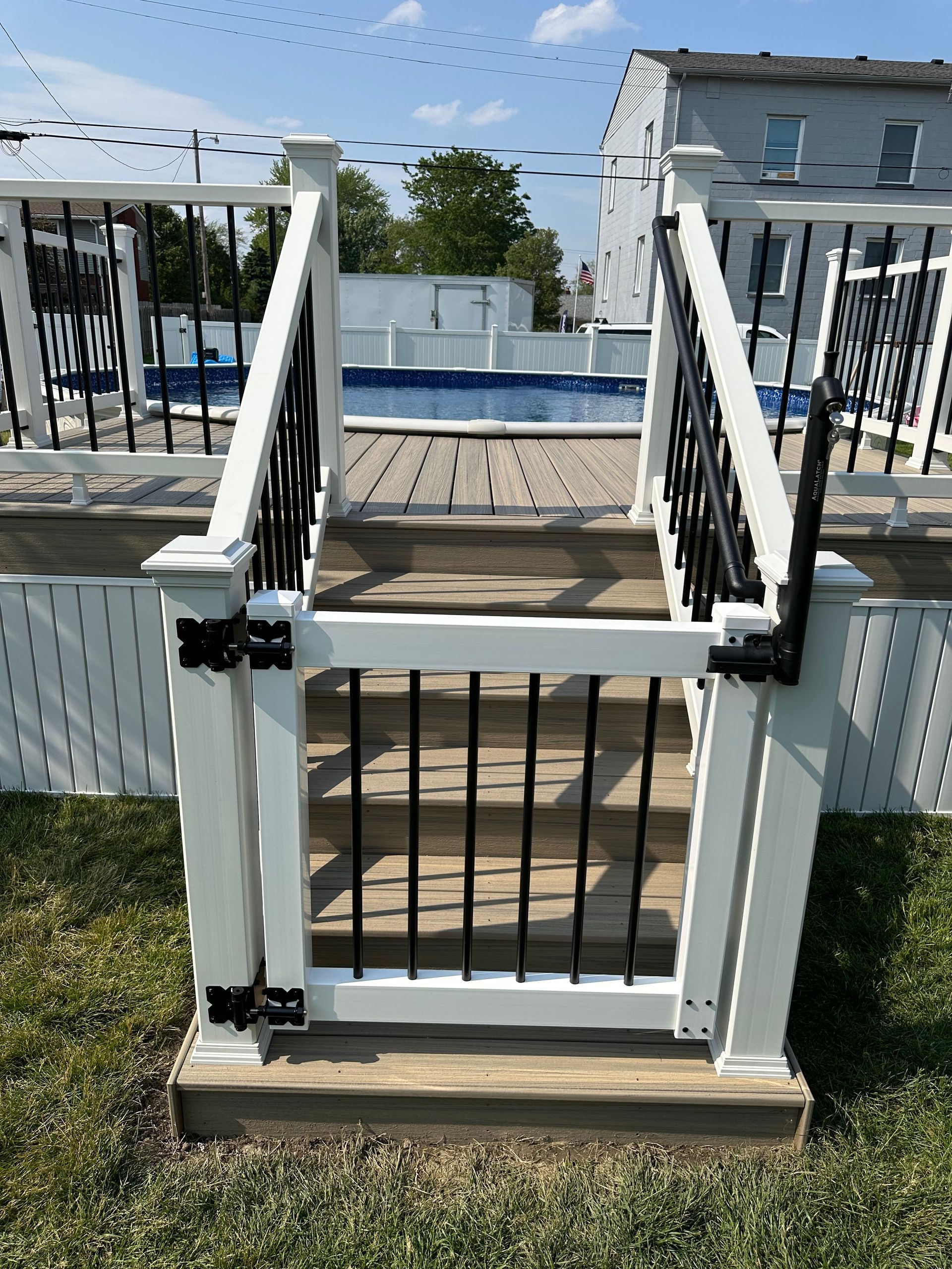 White and black gated deck with a pool in the background.