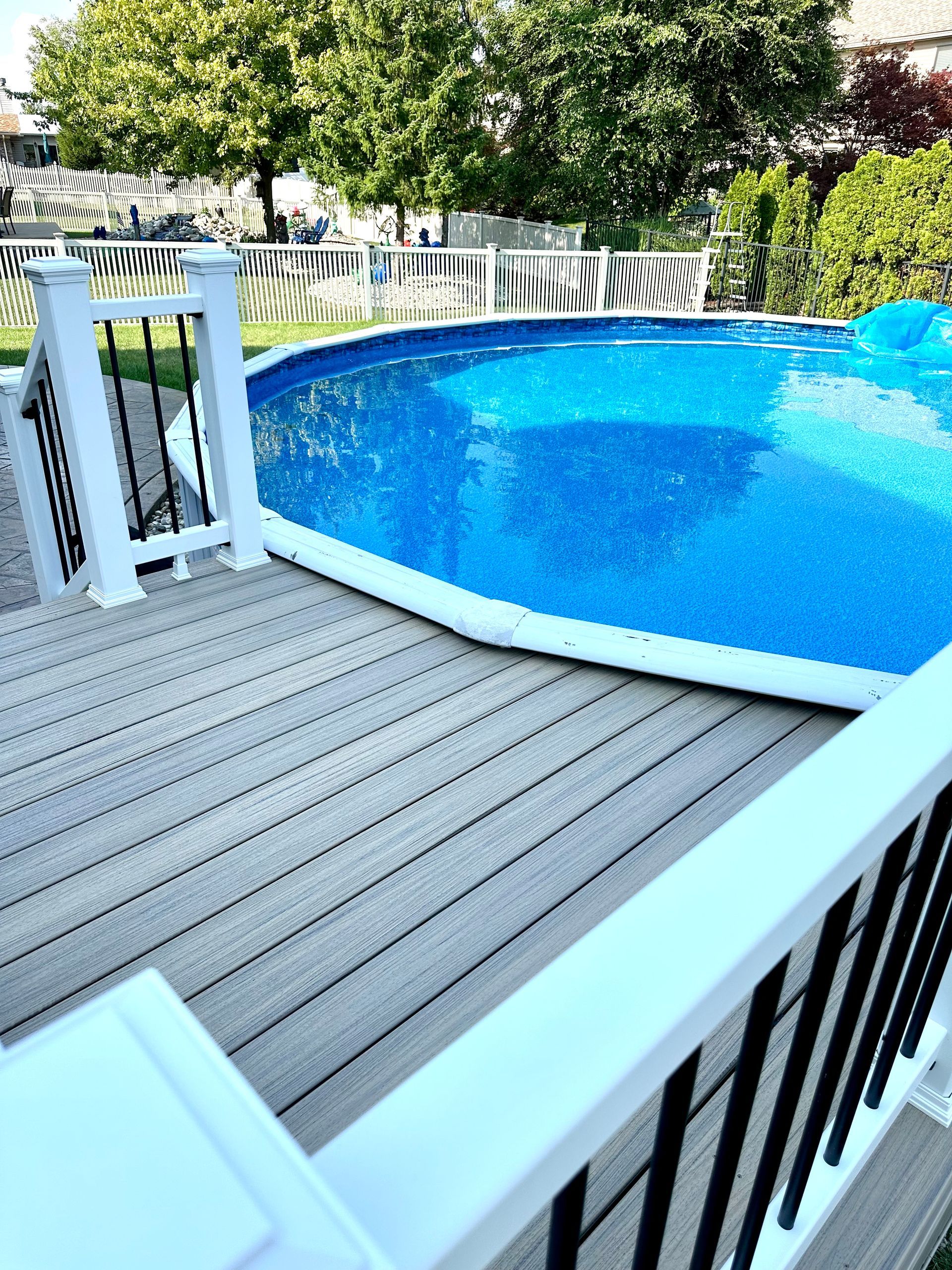 A backyard with a composite deck surrounding a blue above-ground swimming pool.
