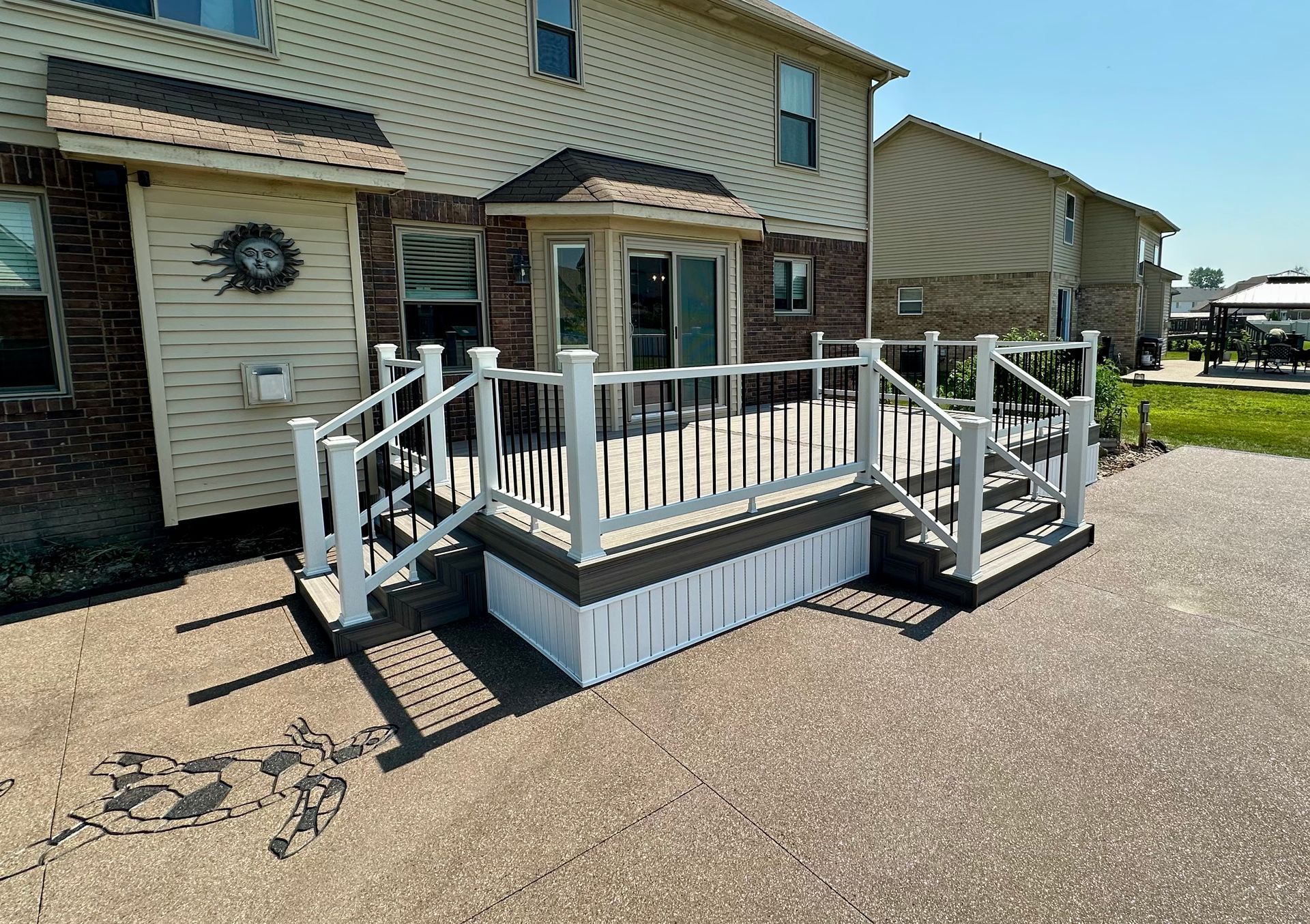 Deck with white railing and steps attached to a two-story beige house on a sunny day.