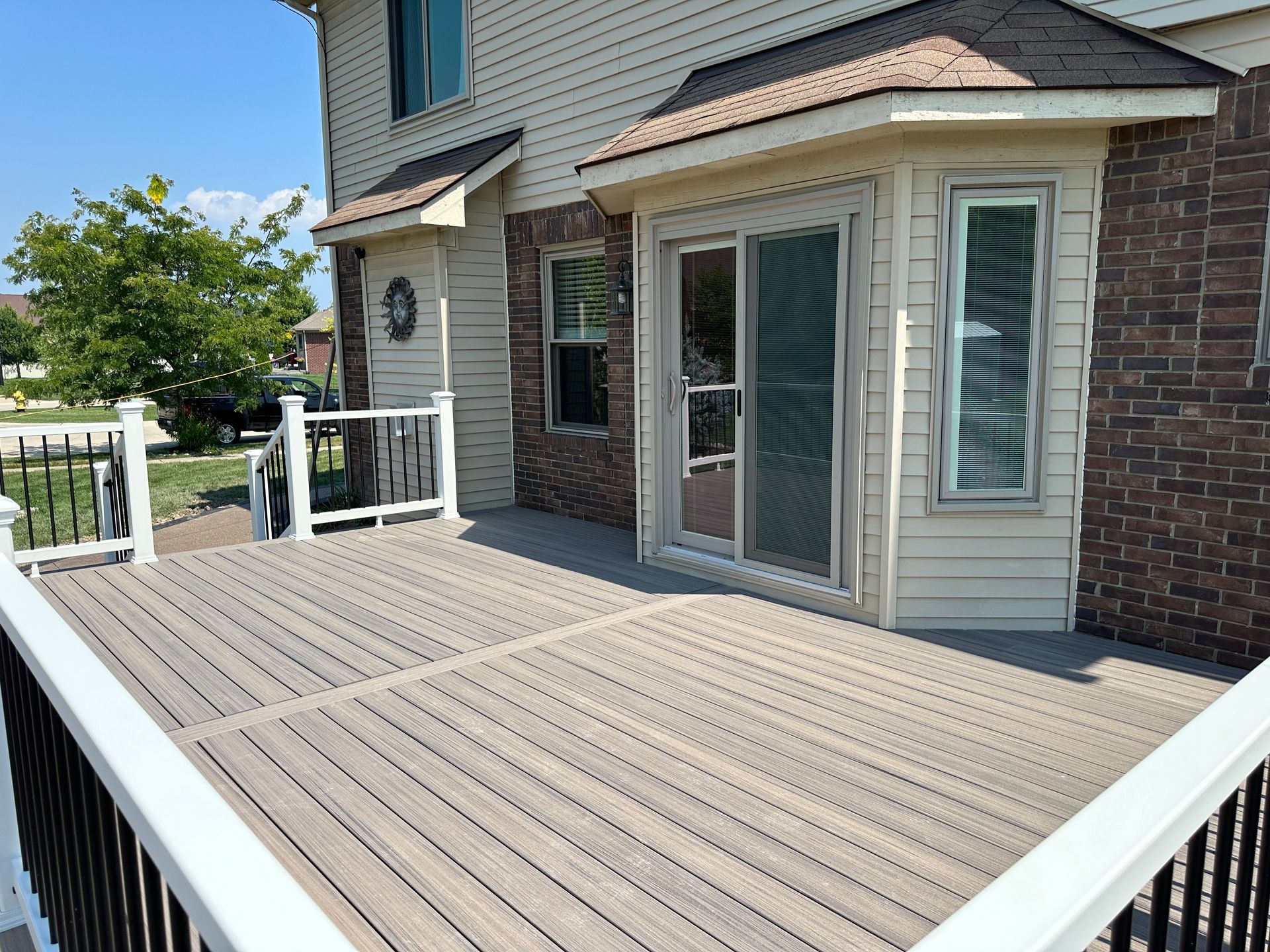 Composite deck with white railings next to a two-story brick house with a sliding glass door.