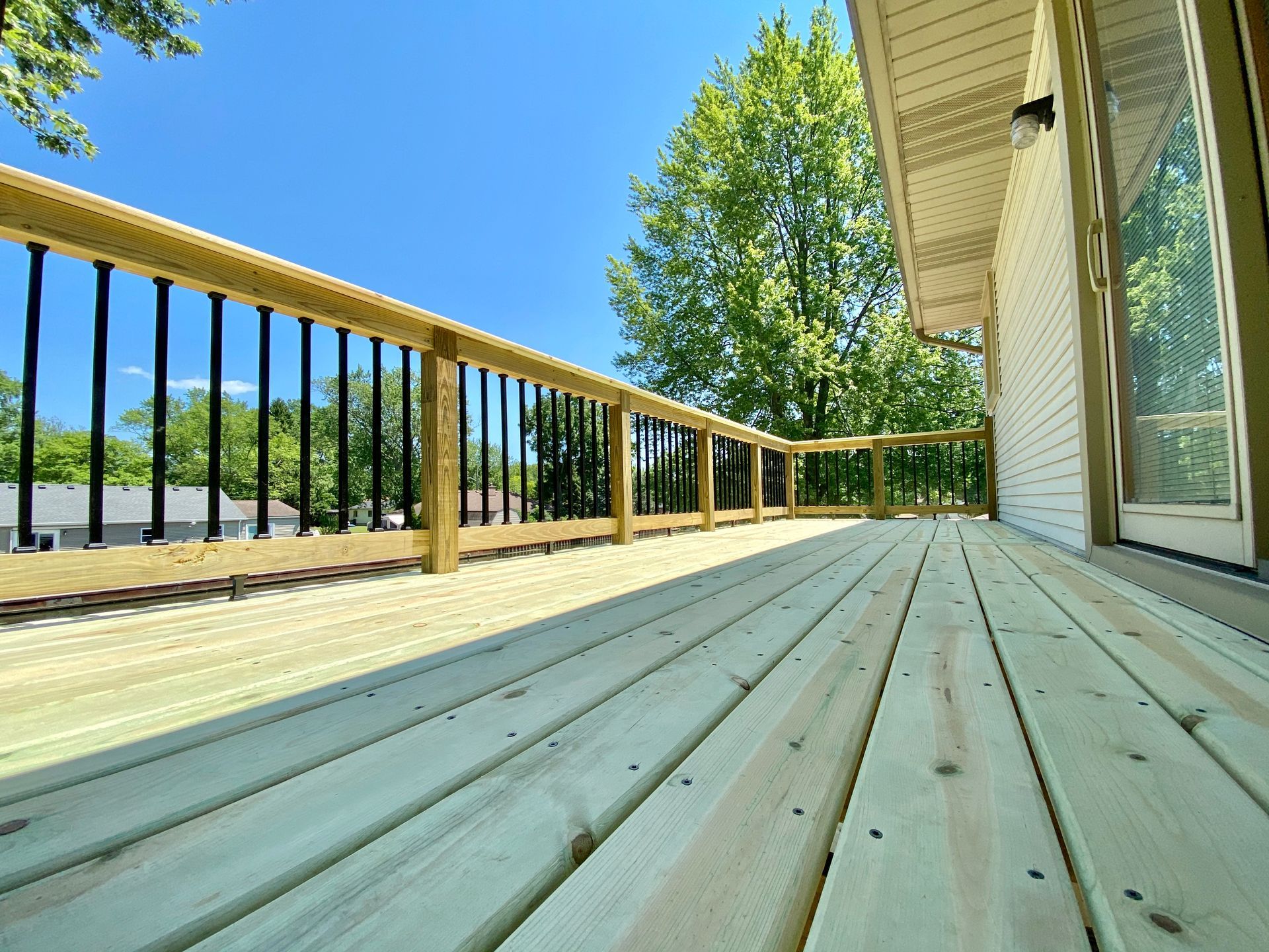Wooden deck with black railings and light-colored siding on a sunny day.