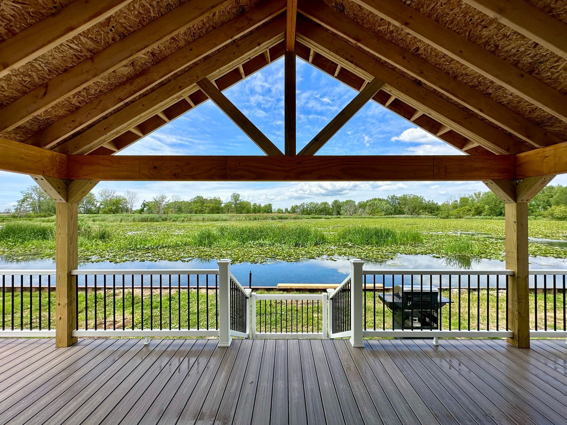 Gazebo overlooking a lake with lily pads. Wooden structure with a view of water and greenery.