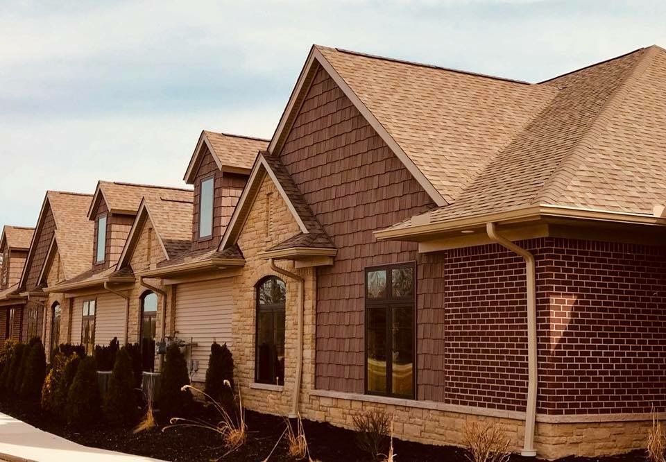 Row of houses with brown roofs, tan siding, and brick accents against a cloudy sky.