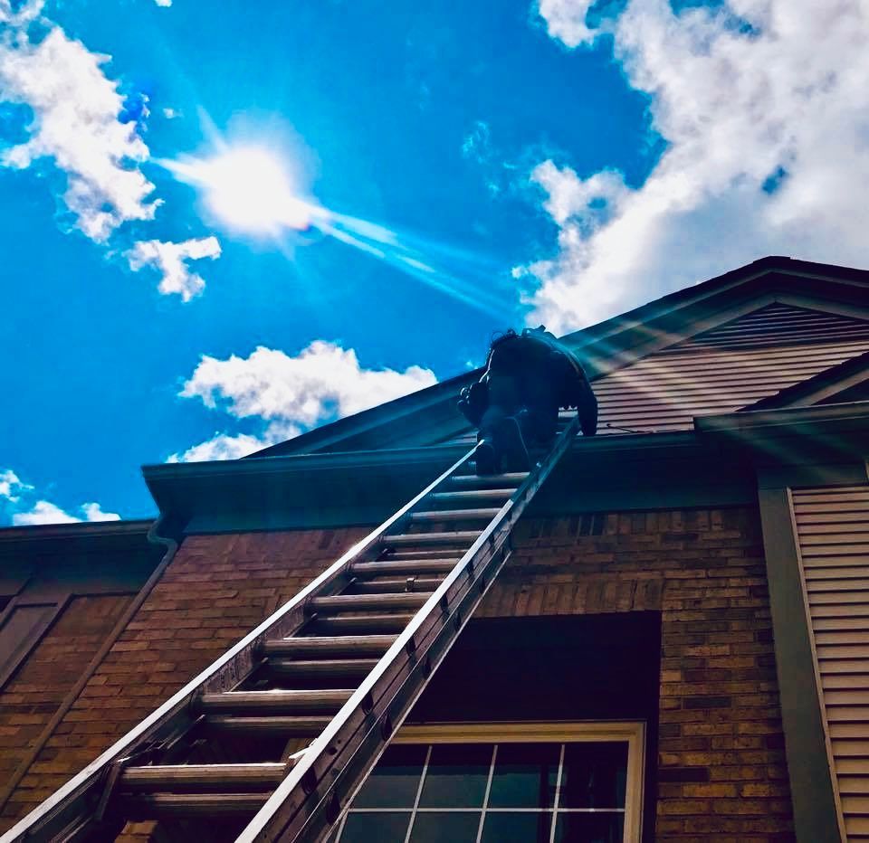Person on a ladder, working on a roof. Bright sun in a blue sky.