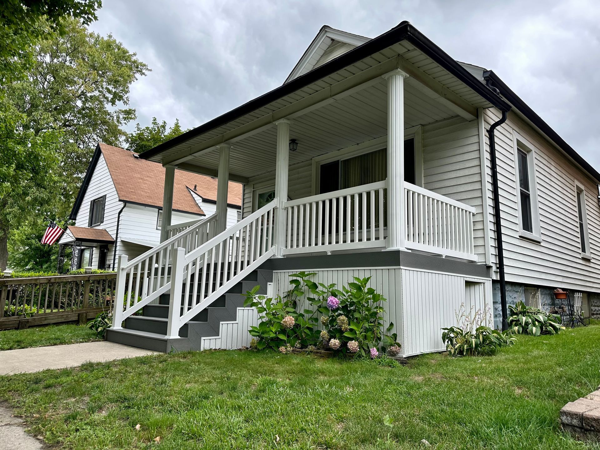 White house with porch, gray steps, and green lawn under a cloudy sky.