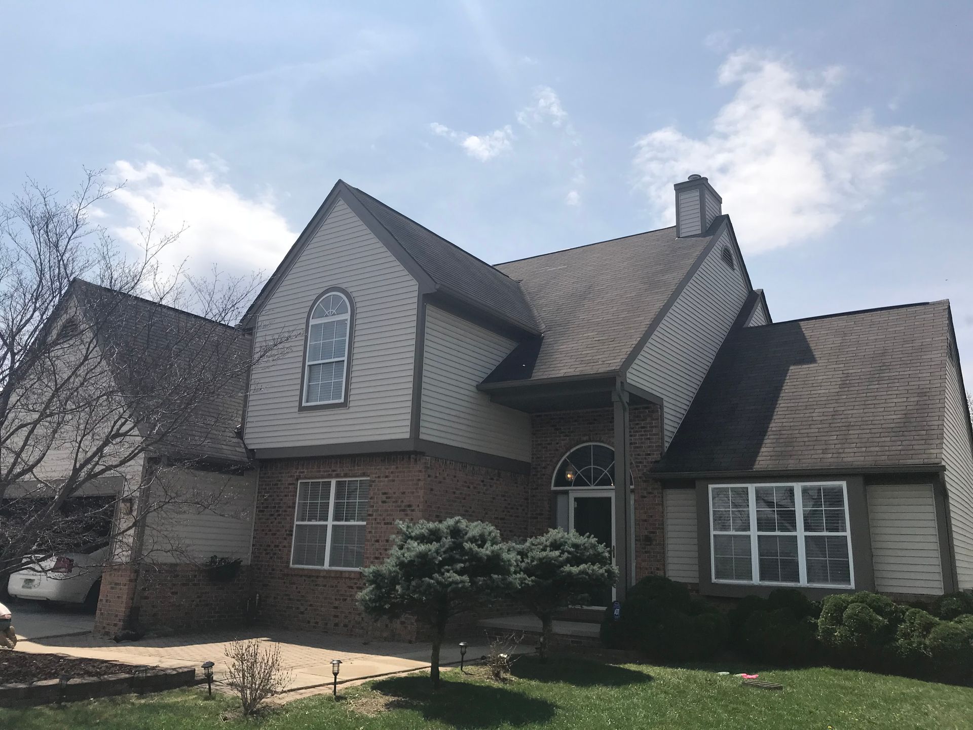 Two-story house with brick and siding, a dark roof, and arched windows under a partly cloudy sky.