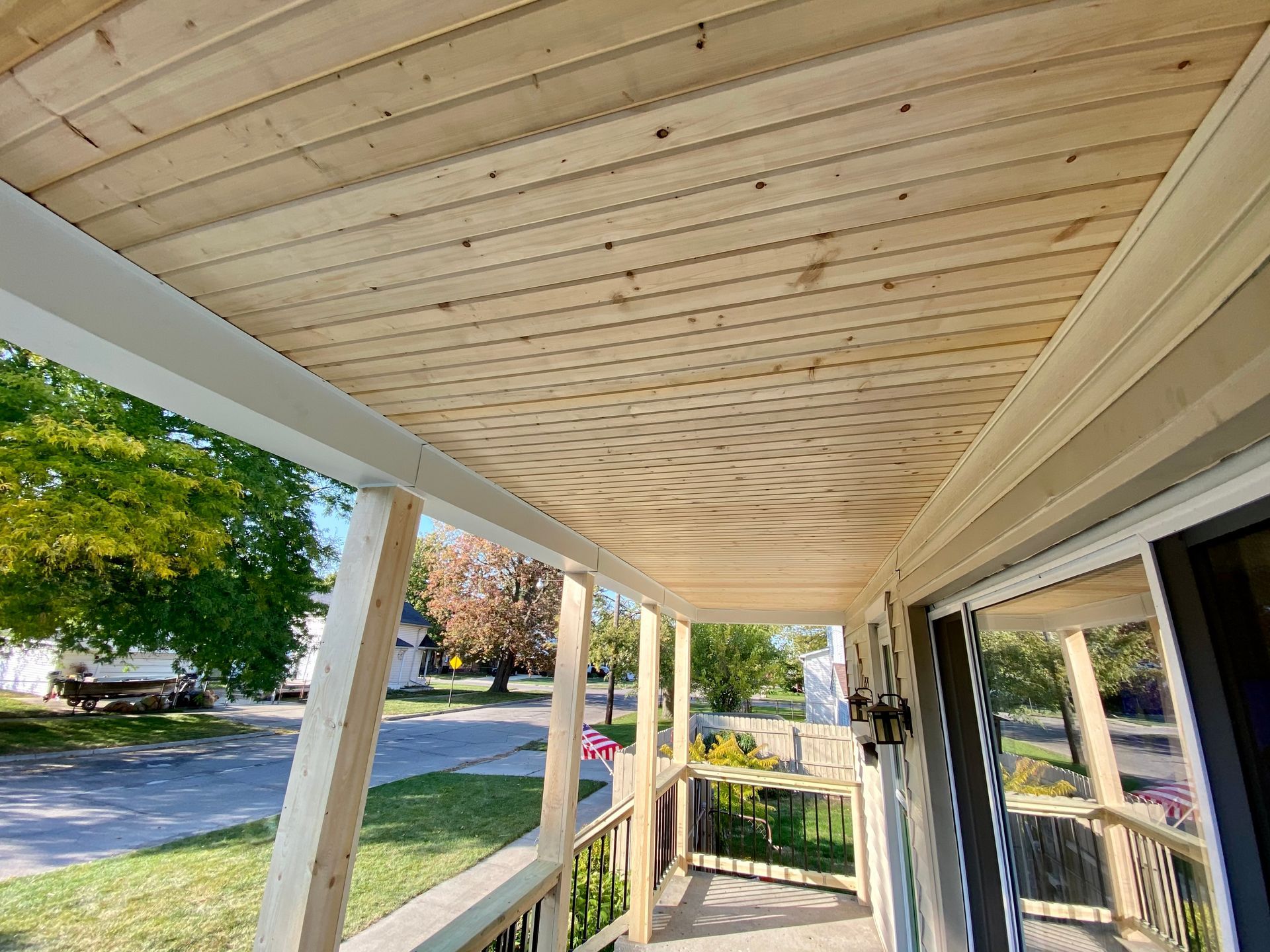 Porch ceiling with natural wood planks, supported by white posts. The view is looking up at the ceiling.