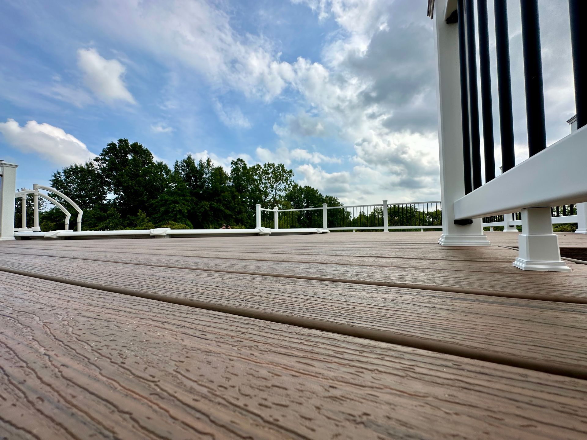 Wooden deck with white railing, black vertical posts, and a cloudy sky in the background.