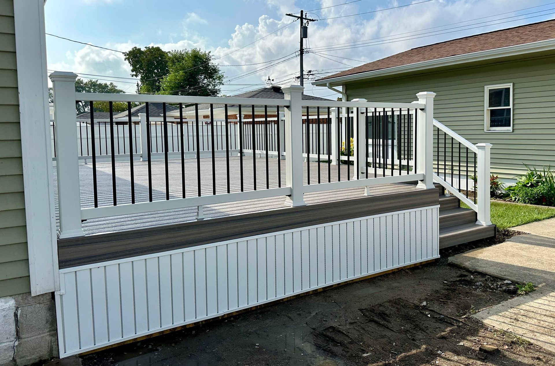 White deck with black railings attached to a green house, sunny day.