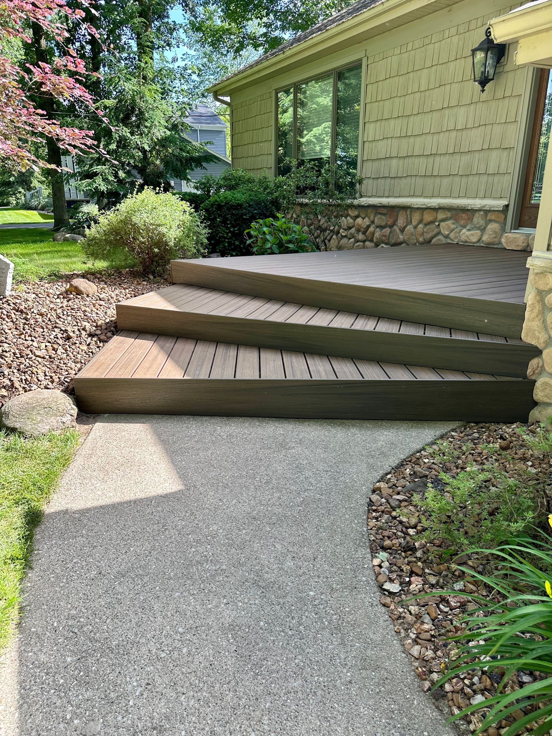 A stone and wood front porch with steps leading to a house, a walkway, and landscaping.