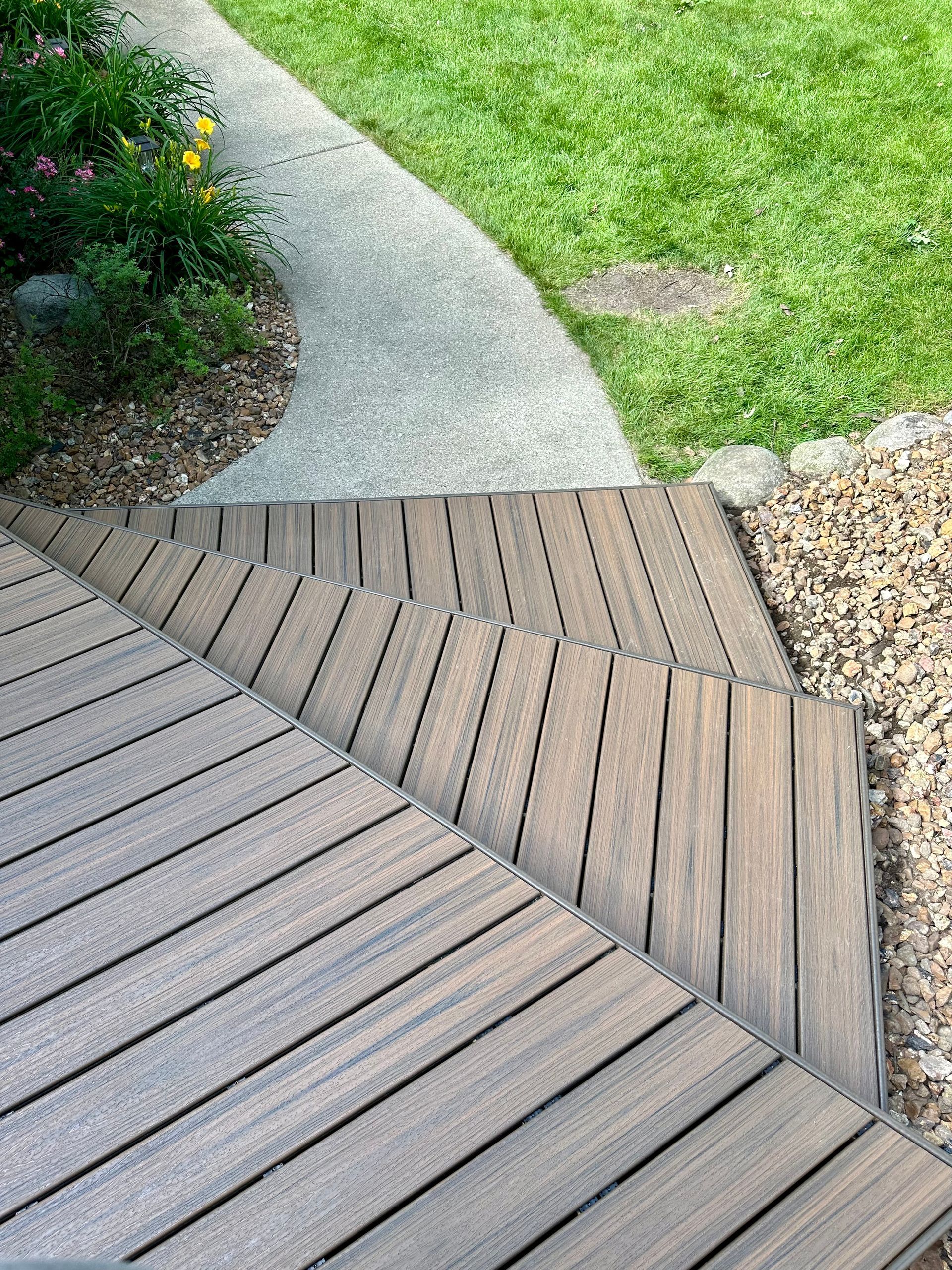 Wooden steps leading down to a curving concrete path and grassy lawn.