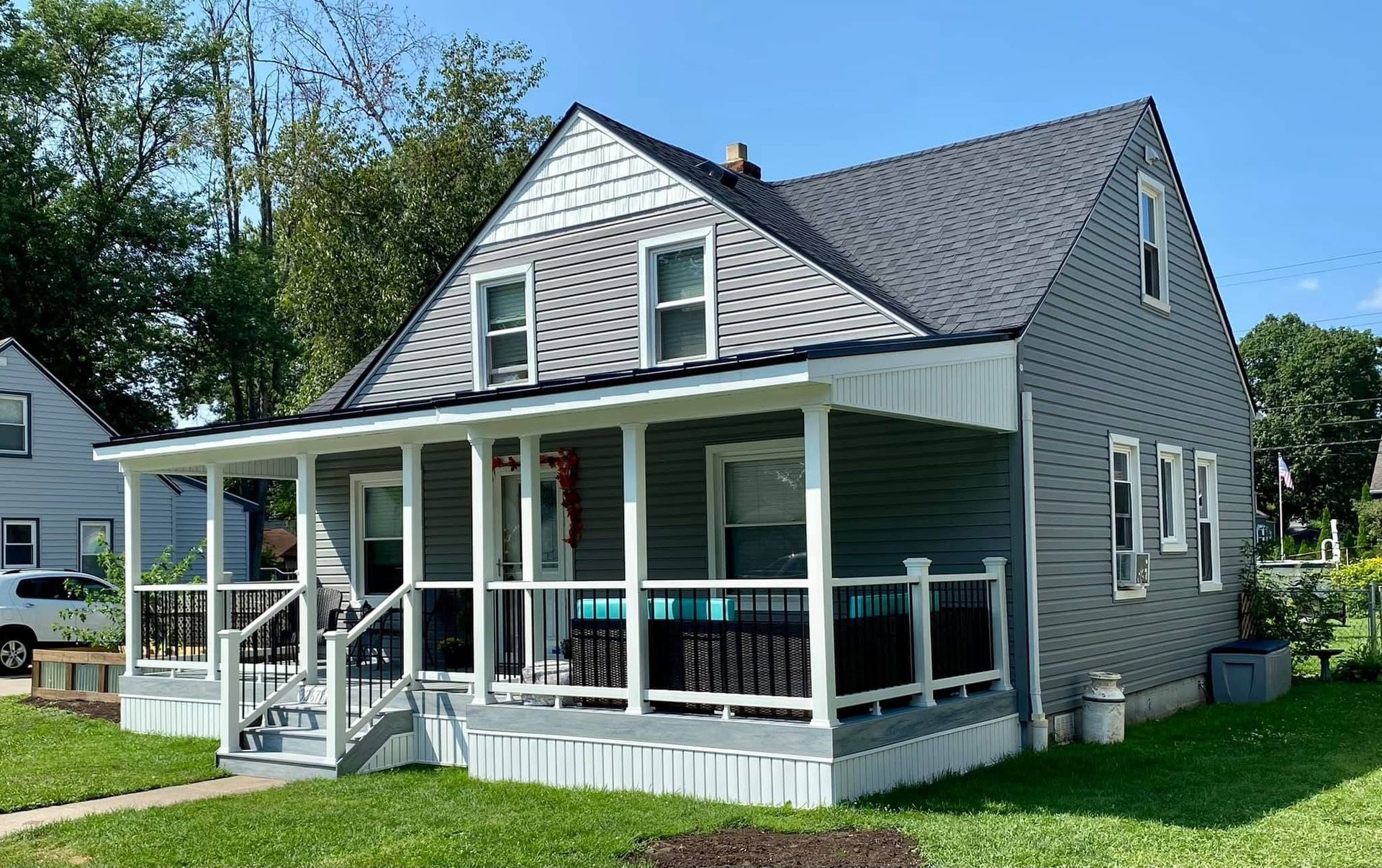 Gray house with a porch, white trim, and a black roof. Green lawn under a blue sky.