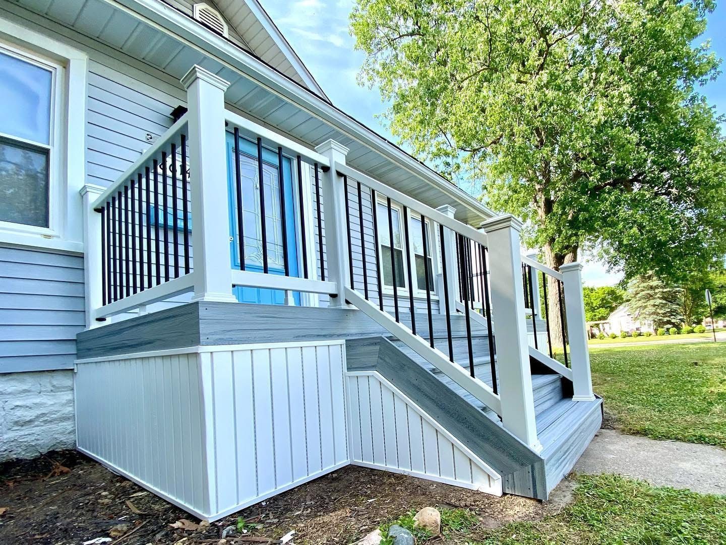 Gray and white house porch with stairs and black railing; sunny day.