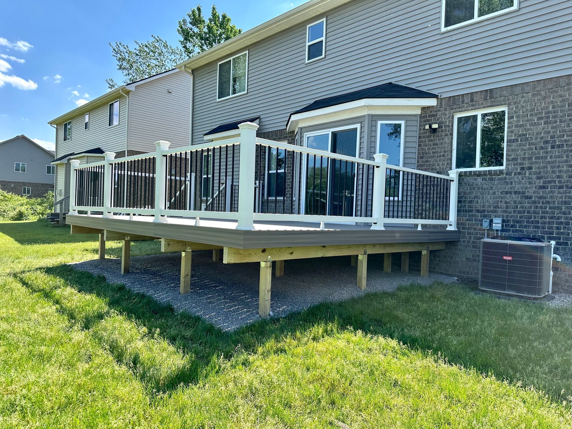 Backyard deck with white railing and dark balusters, attached to a two-story gray house.