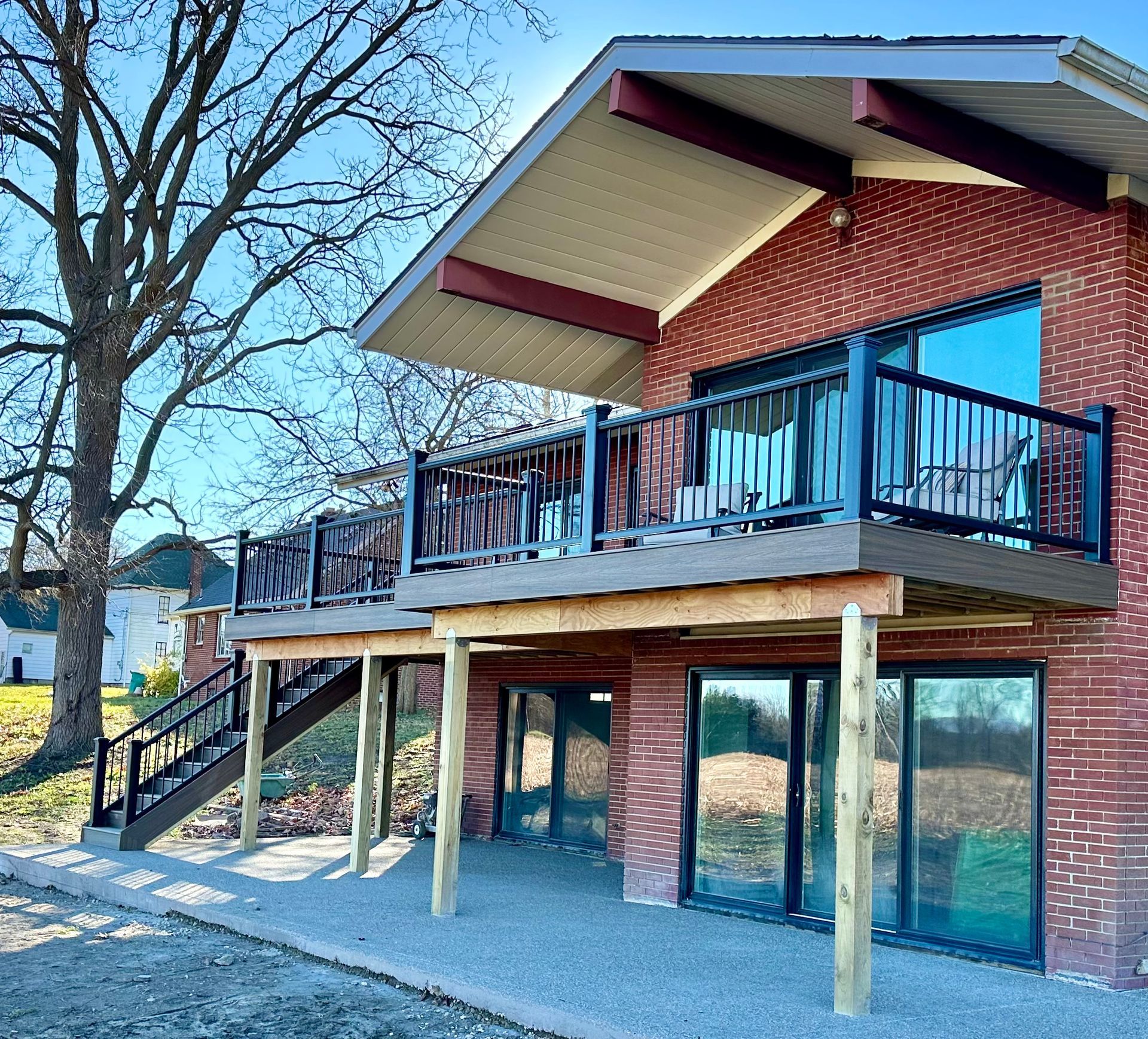 Brick house with second-story deck, stairs, and large windows. Beige posts support the deck; blue sky.