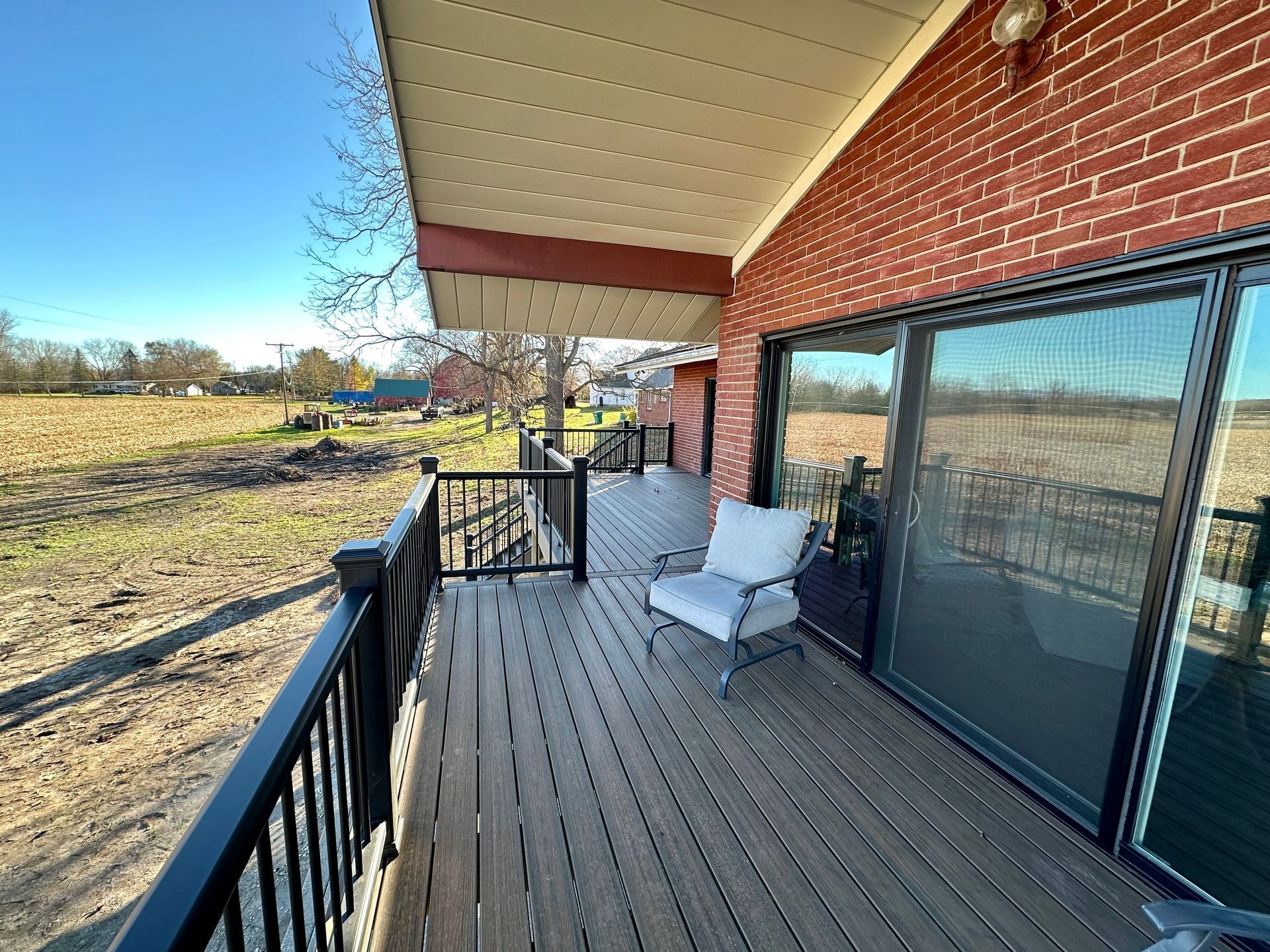 Deck with a chair next to sliding glass doors, red brick wall, and a field.