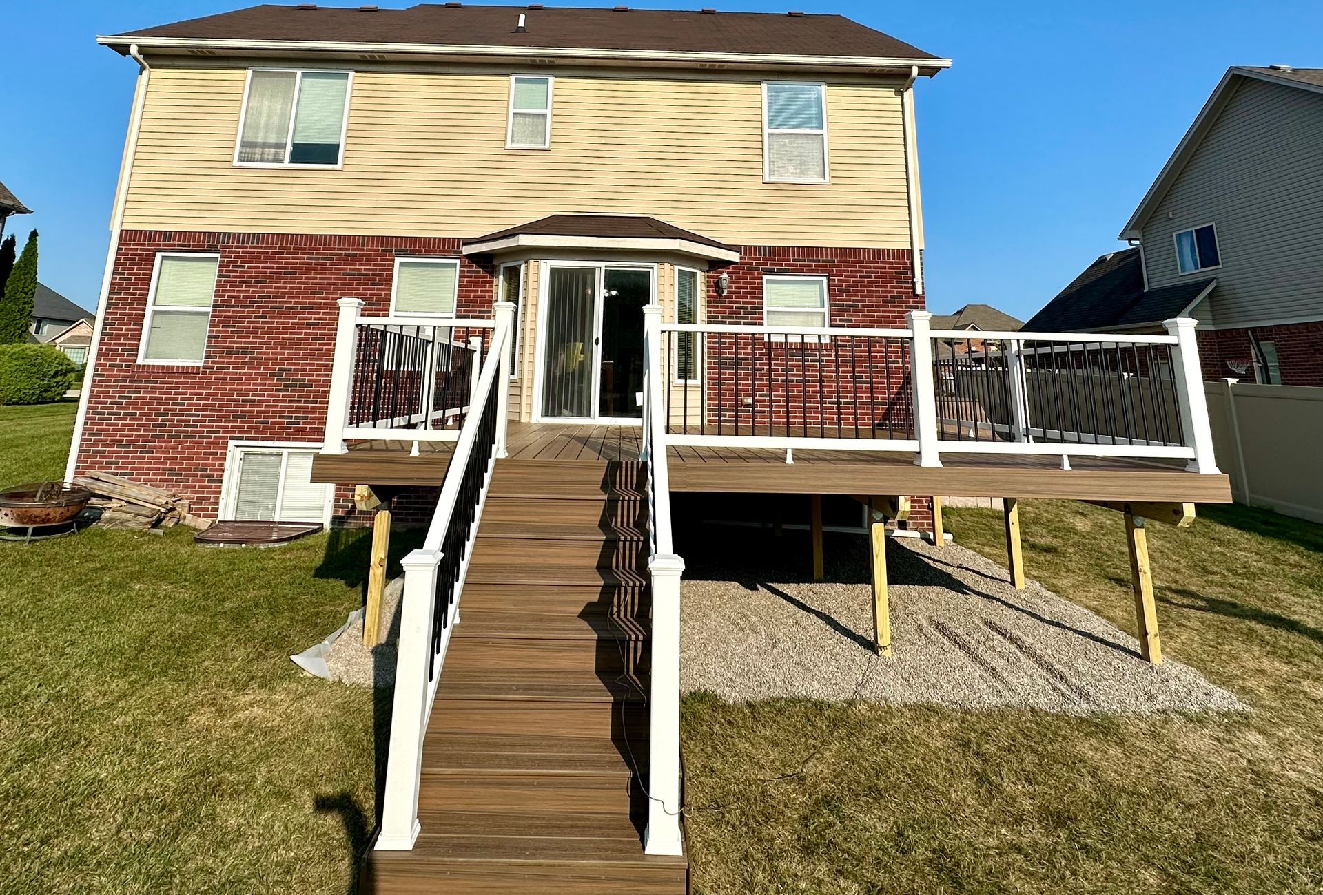 Rear view of a two-story house with a wooden deck and stairs leading down to the yard with gravel.