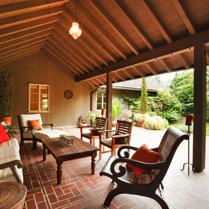 Covered outdoor patio with brick floor, wood furniture, and garden views.