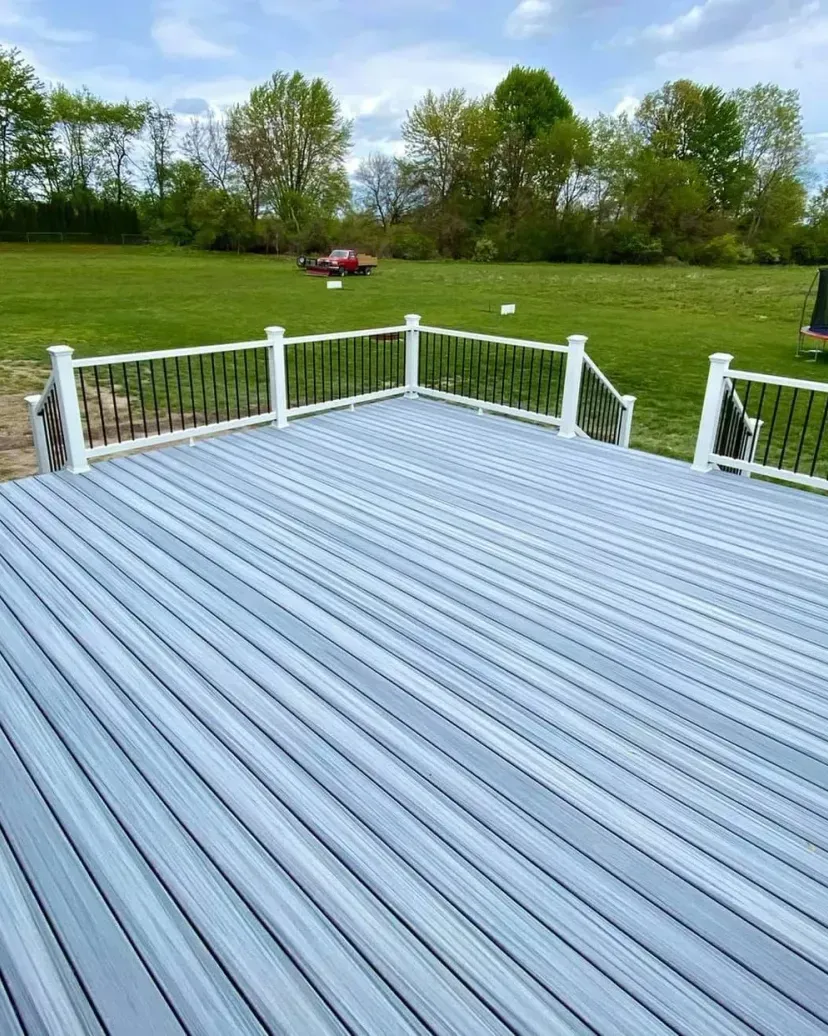 Gray composite deck with white posts and black railings, overlooking a green lawn.