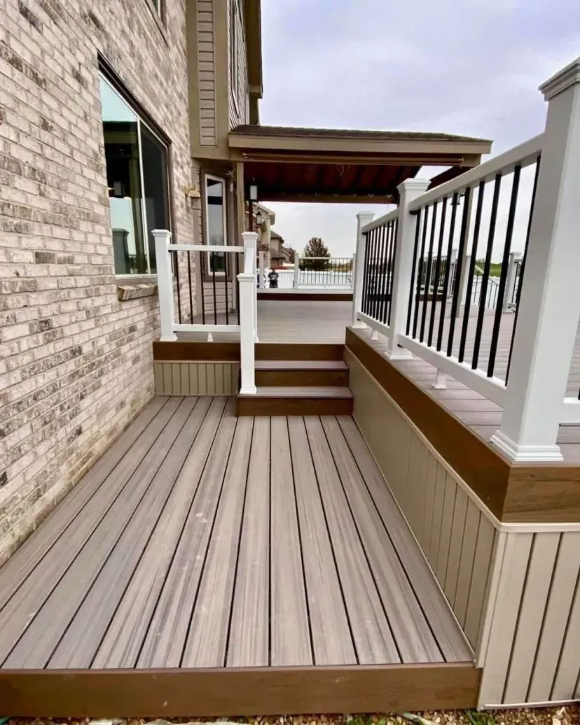 Composite deck with stairs and railings against a brick building; neutral tones.