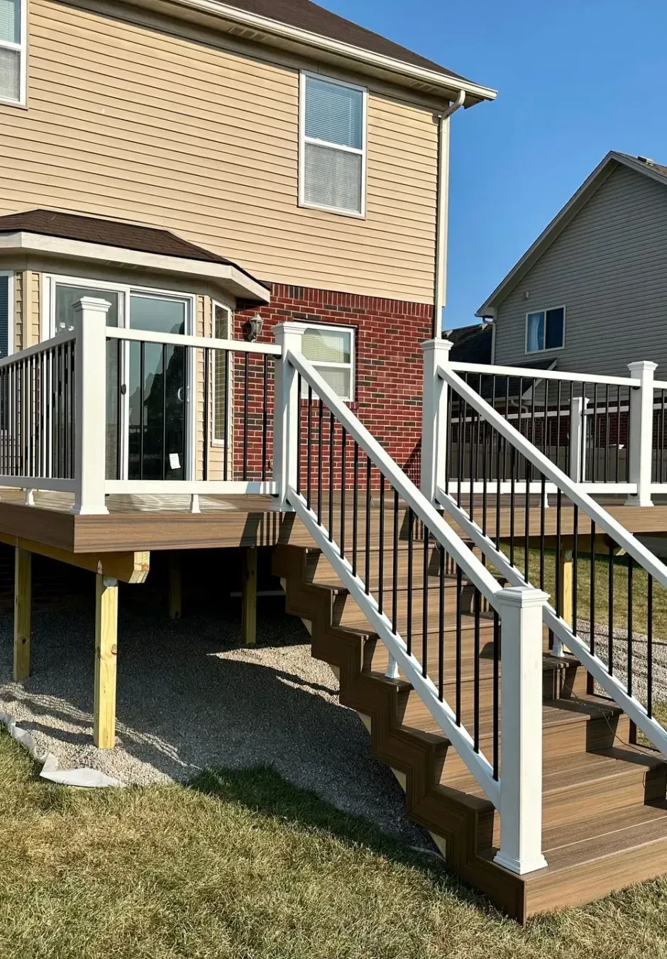 Backyard with a raised deck, stairs, white railing, and a tan and brick house.