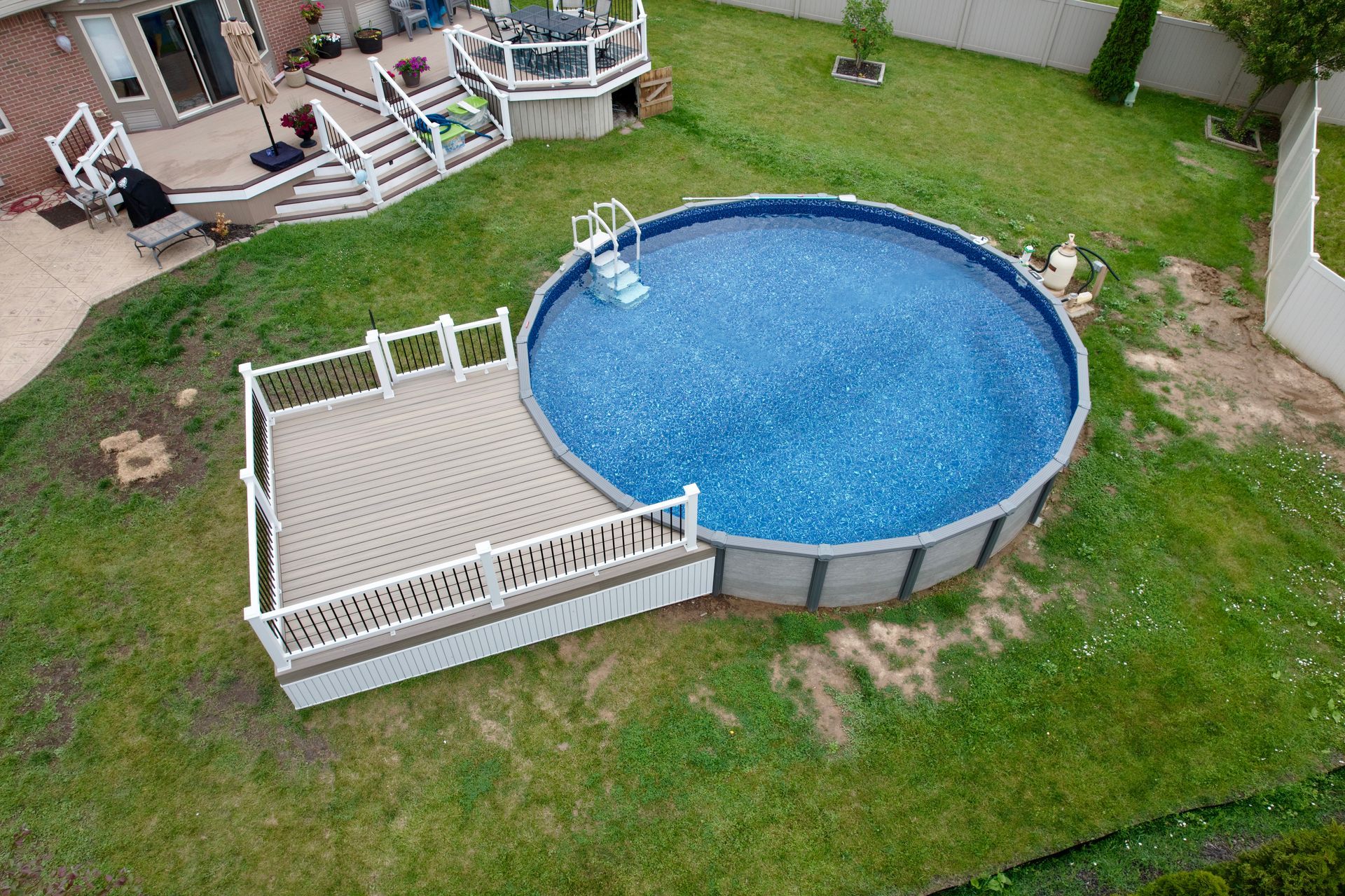 Aerial view of an above-ground pool with attached deck in a grassy backyard.