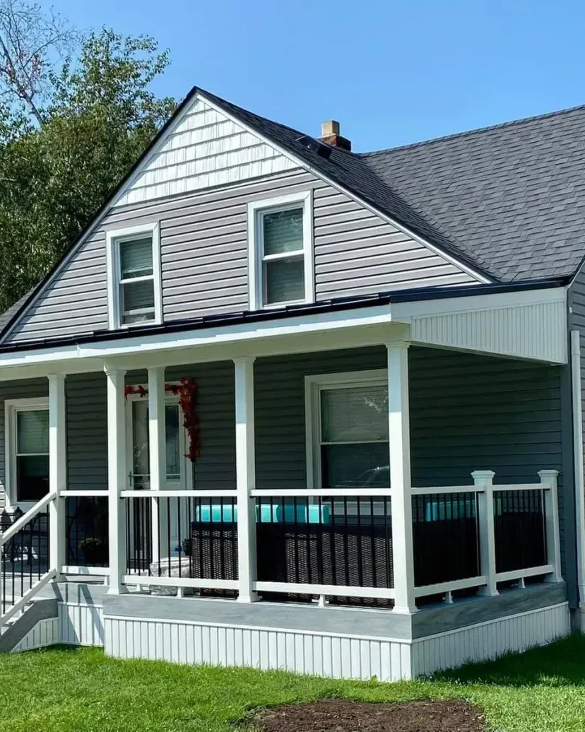Gray house with white trim, porch, and a dark shingled roof under a clear blue sky.