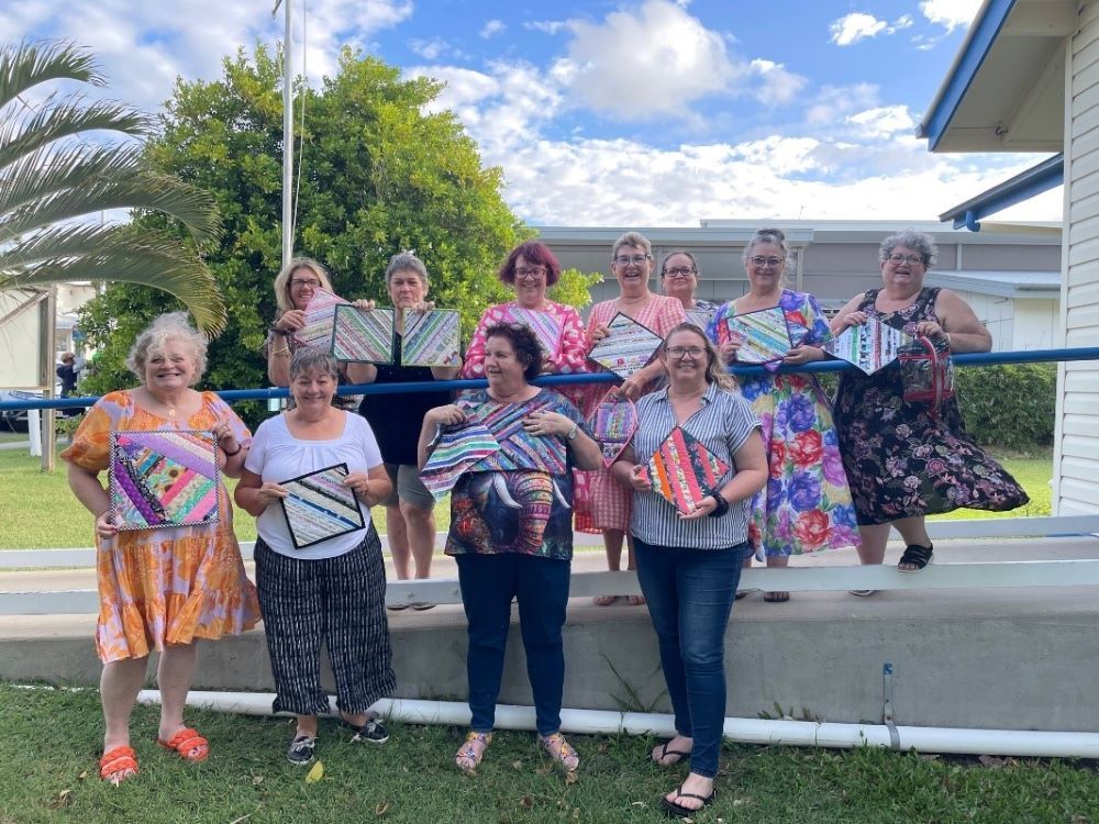 A Group of Women Are Standing Next to Each Other Holding Quilts — Lyn-Jelle Crafts in Emu Park, QLD